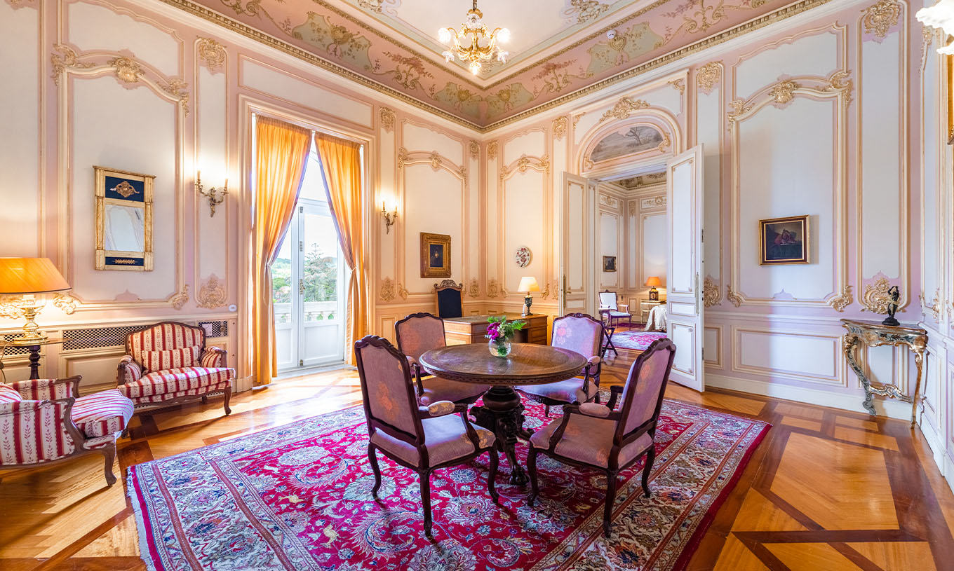 A Suite D. Carlos do Pestana Palace Lisboa tem um salão grande e luxuoso com uma janela e mesa para refeições