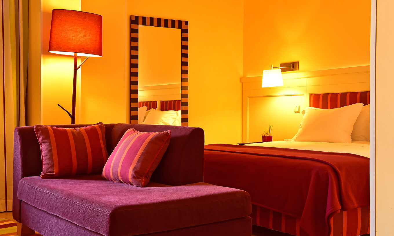 A Junior Suite do Pestana Sintra Golf tem uma cama de casal, uma espelho na parede e um pequeno sofá vermelho