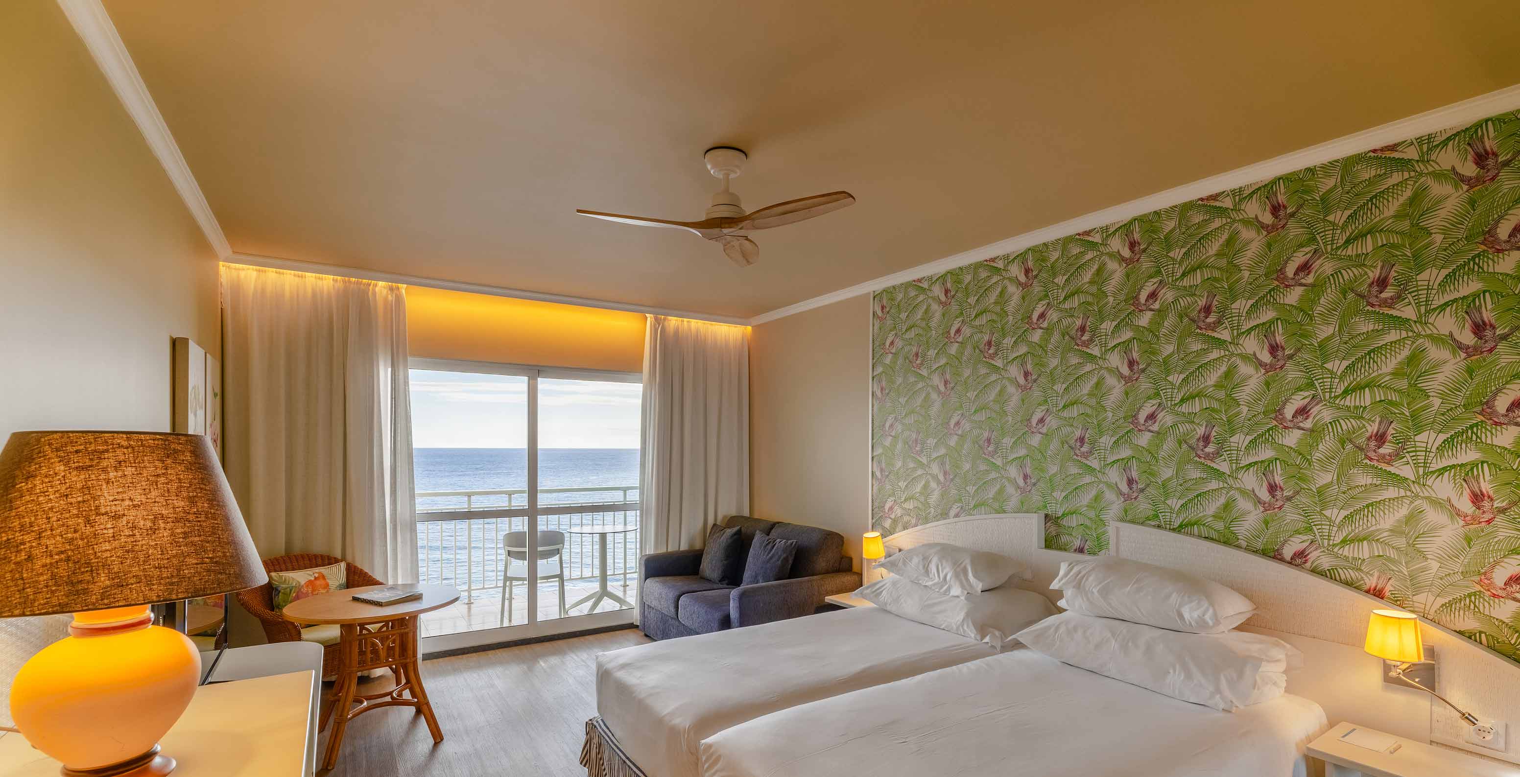 O Premium Sea View do Pestana Ocean Bay All Inclusive tem uma cama dupla, papel de parede com palmeiras, um sofá e varanda