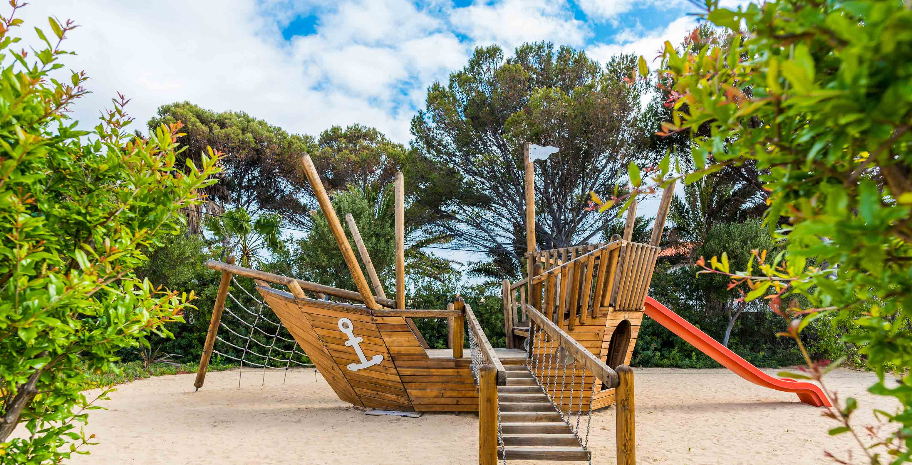 Parque infantil com um grande barco pirata de madeira, escorrega vermelho e rede de escalada no Pestana Porto Santo
