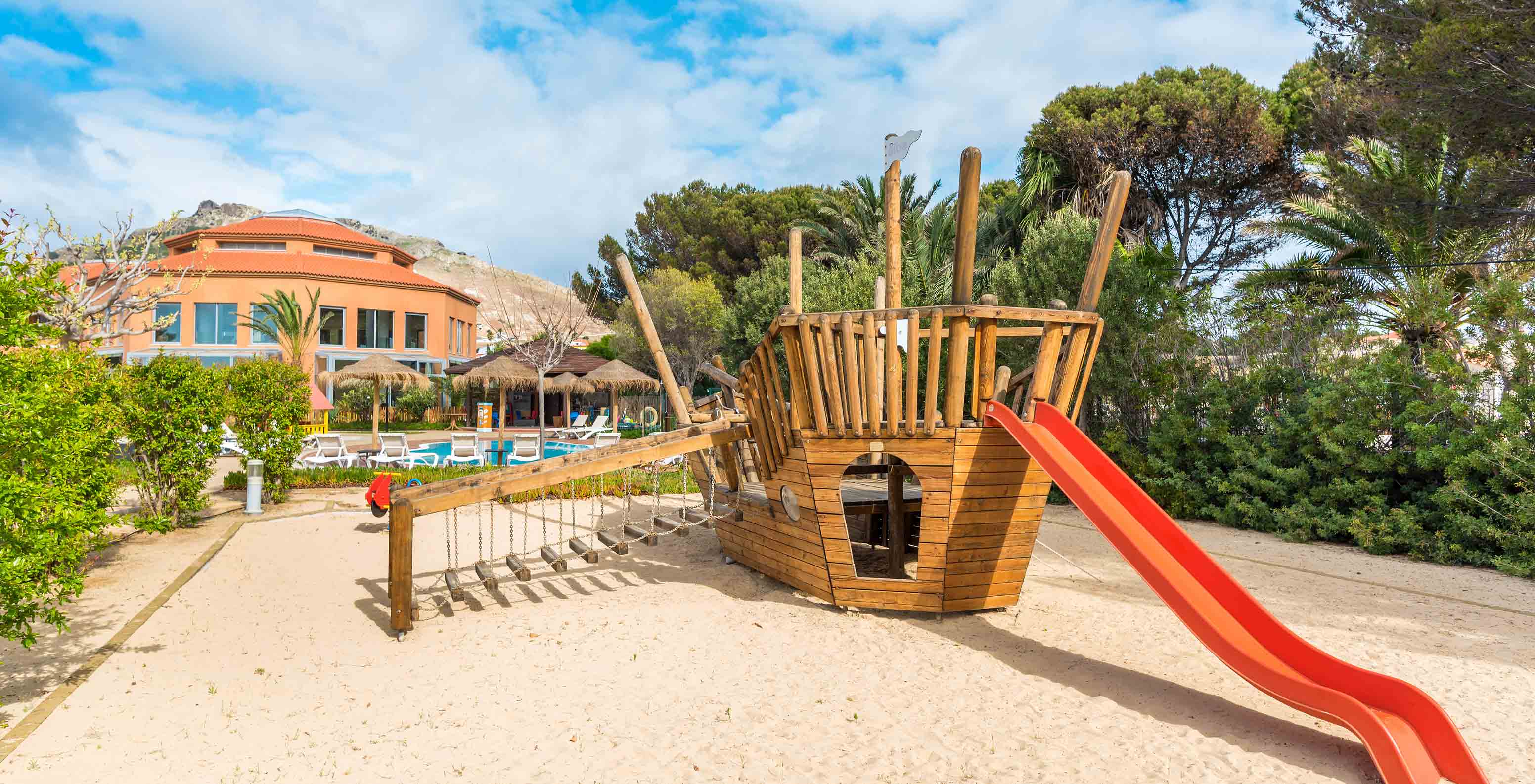 Parque infantil no Pestana Porto Santo com um grande barco de madeira, escorrega vermelho sob um céu azul