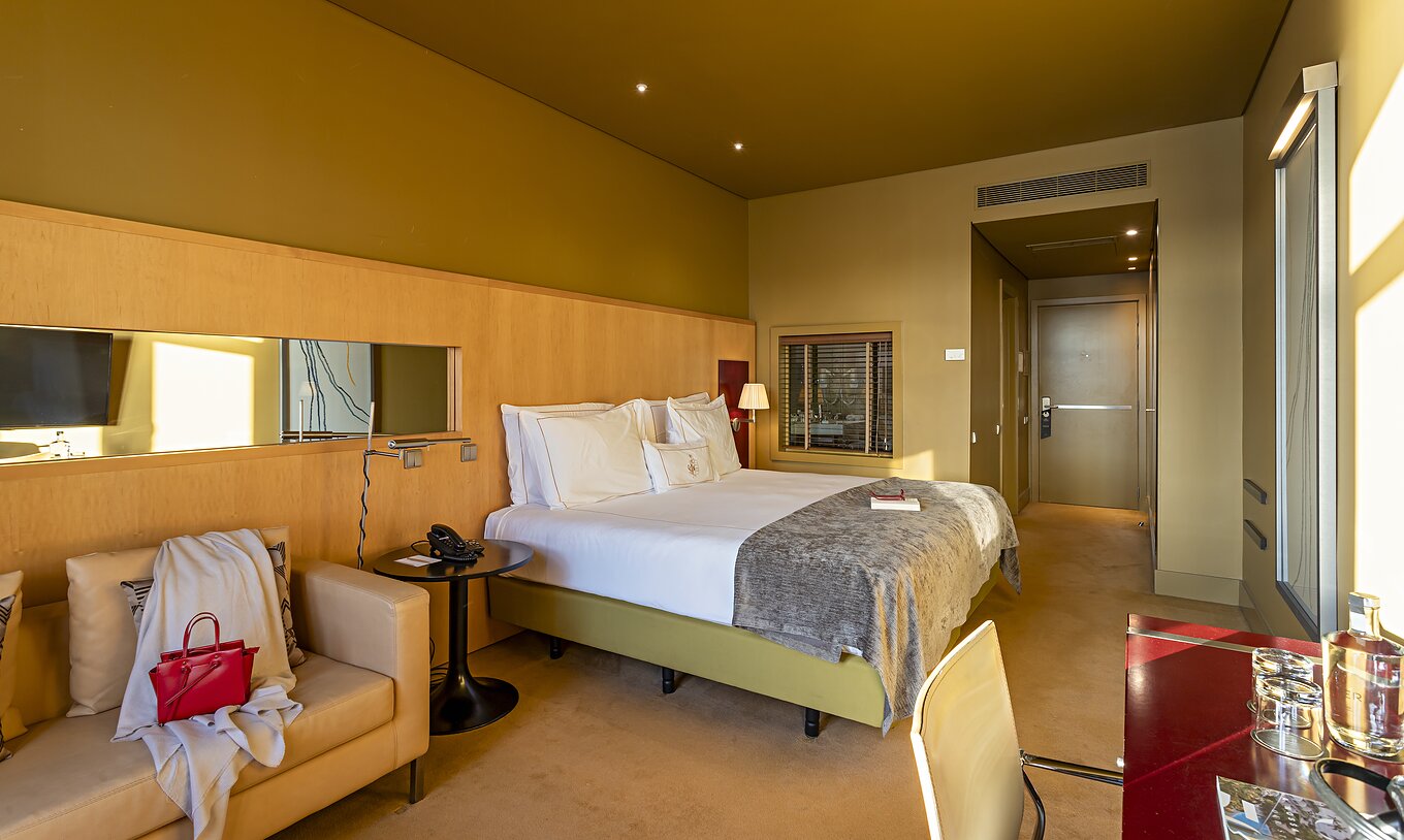 O Executive Superior do Pestana Palácio do Freixo tem uma cama de casal, um sofá e uma secretária vermelha