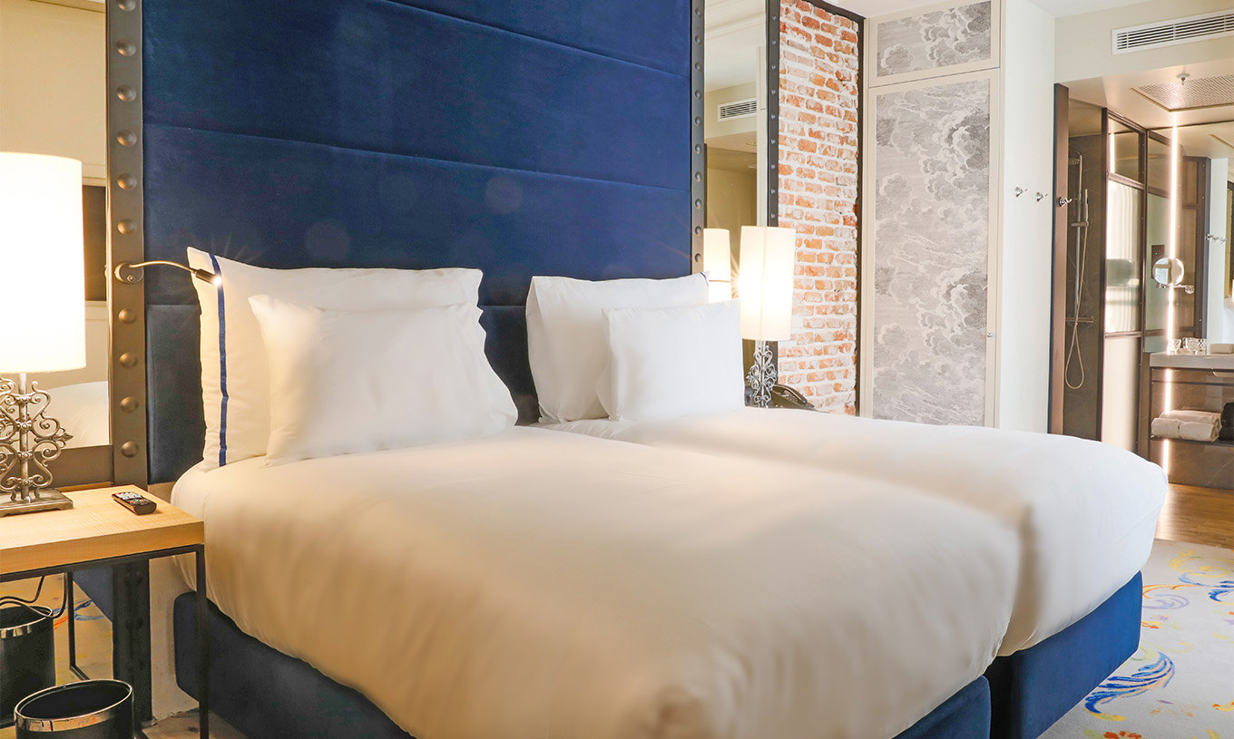 O Quarto Superior do Pestana Plaza Mayor Madrid tem duas camas com cabeceira azul e uma parede com tijolos