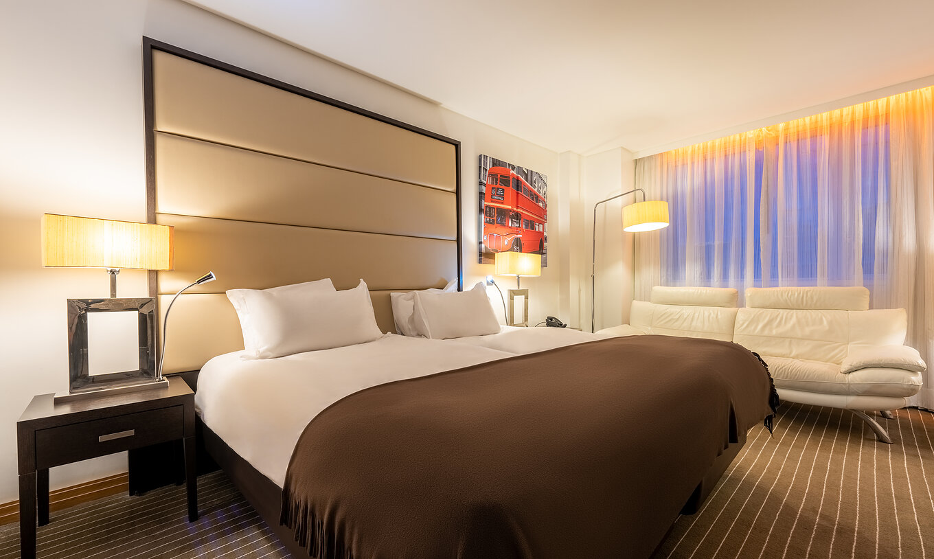 O Premium Twin do Pestana Chelsea Bridge tem duas camas juntas, mesa de cabeceira, sofá, candeeiros e janelas com cortinados