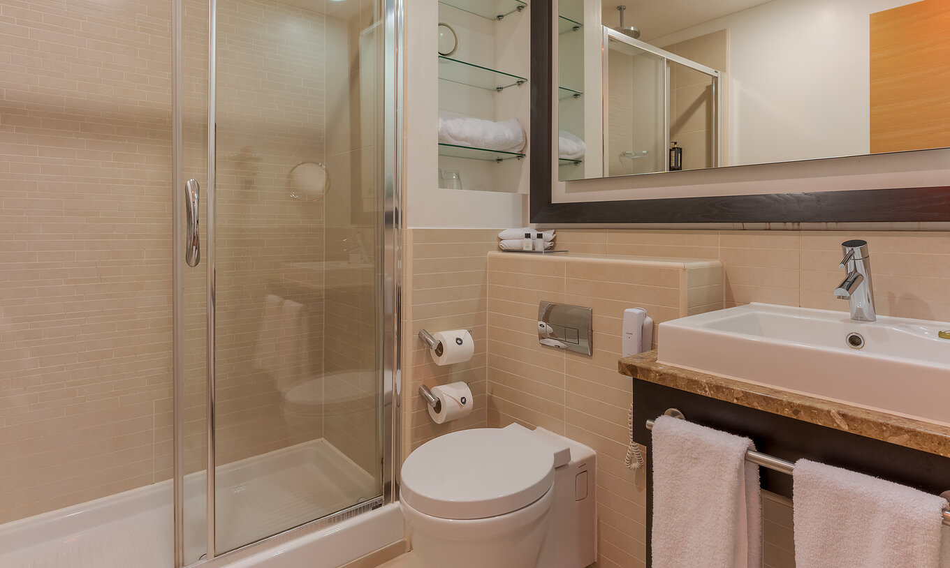 A Executive One Bedroom Suite do Pestana Chelsea Bridge tem duche com portas de vidro, sanita, lavatório e espelho