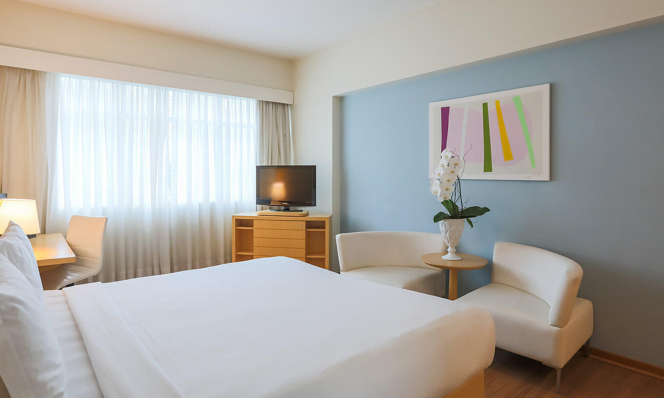 O Queen Luxo Corner do Pestana Curitiba tem uma cama de casal, dois sofás, um móvel com televisão e uma secretária
