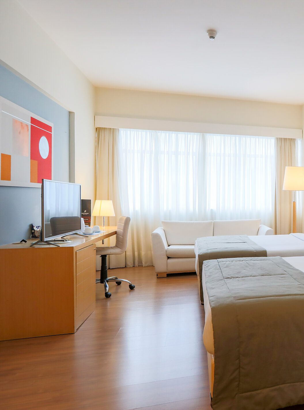 O Quarto Familiar do Pestana Curitiba tem duas camas de casal, uma secretária com televisão e um sofá duplo junto à janela