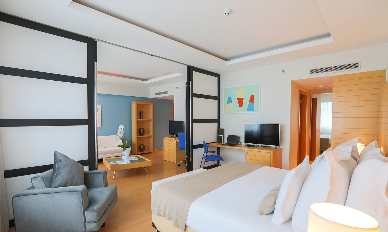 A King Master Suite do Pestana Curitiba tem um quarto com cama king size e uma sala ampla com sofá e televisão