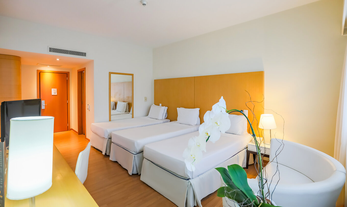 O Twin Luxo Corner do Pestana Curitiba tem três camas individuais com uma secretária com televisão e um pequeno sofá