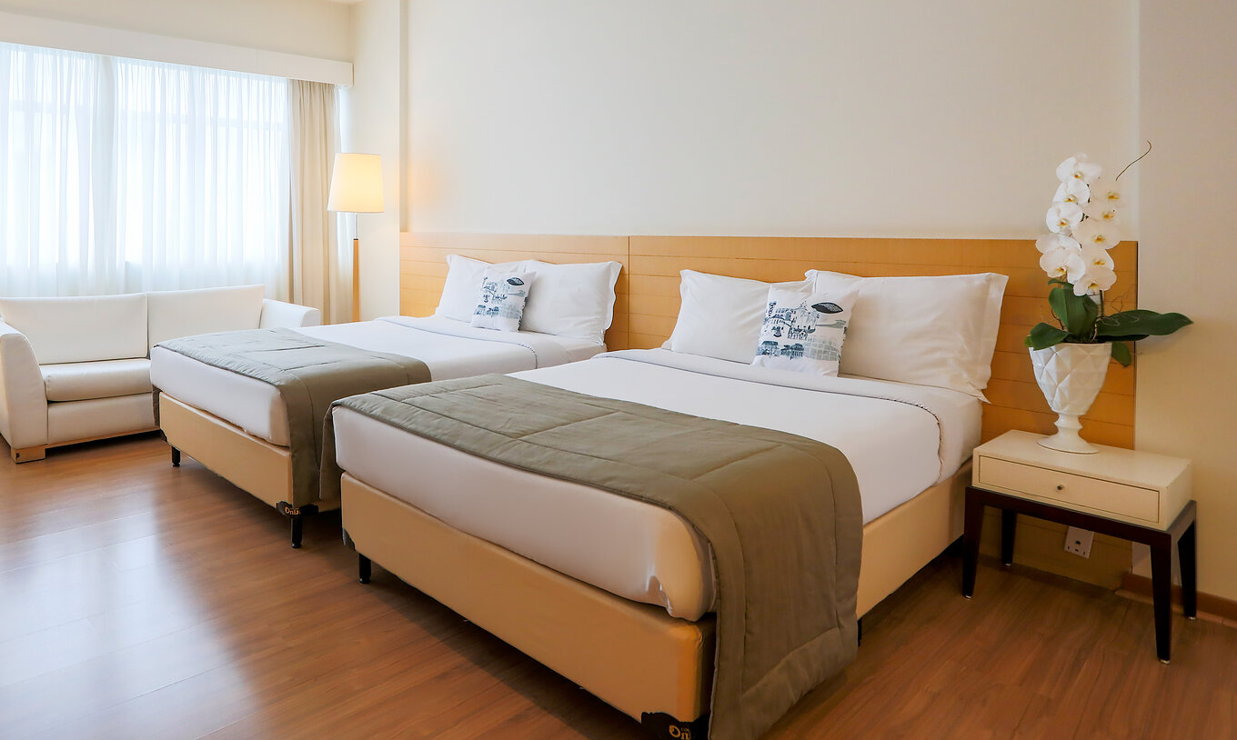 O Twin Superior do Pestana Curitiba tem uma decoração clean em tons de madeira clara, com um sofá duplo e uma janela