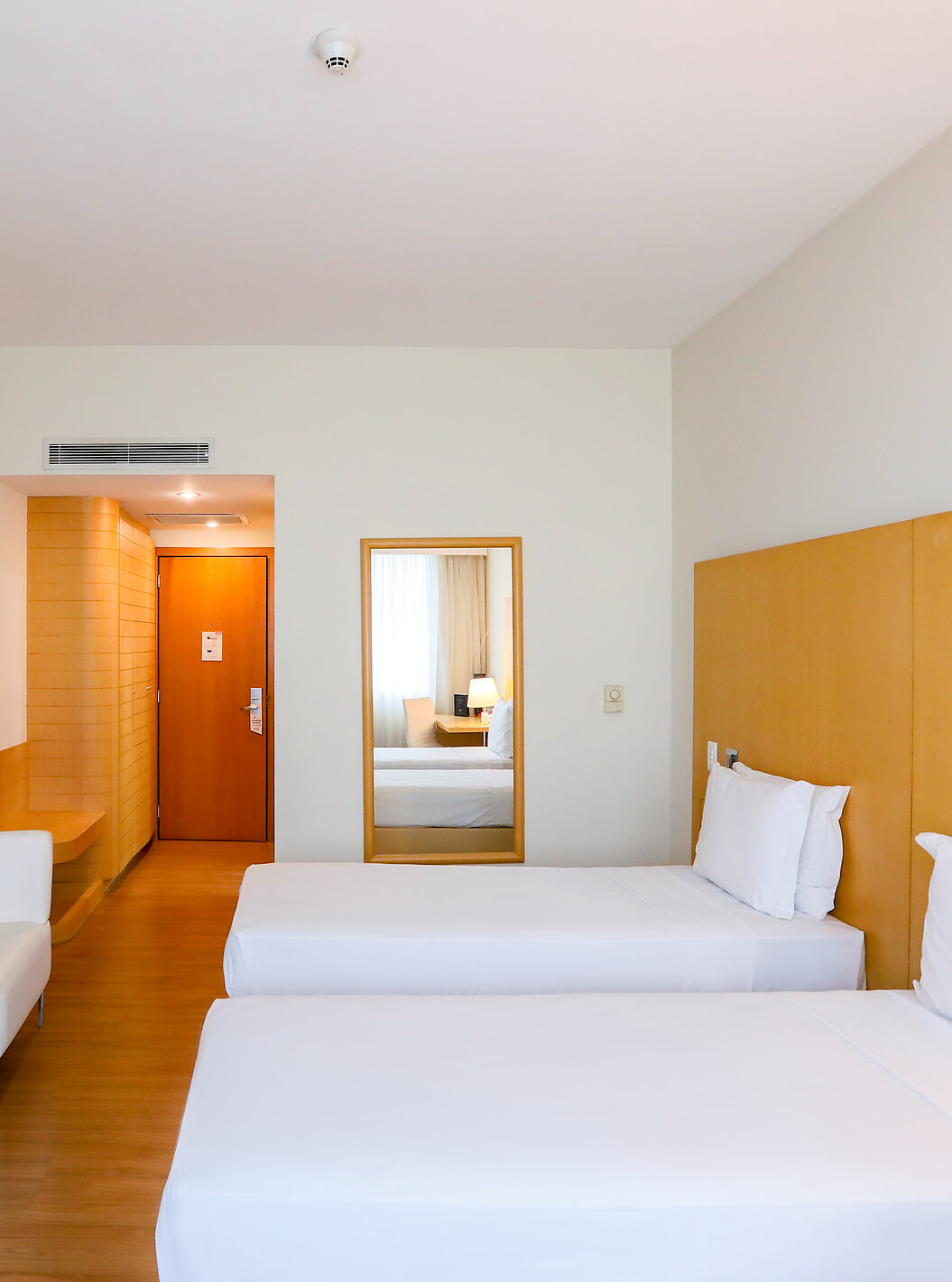 O Twin Superior do Pestana Curitiba tem duas camas individuais com sofás nos pés da cama e uma pequena mesa com flores