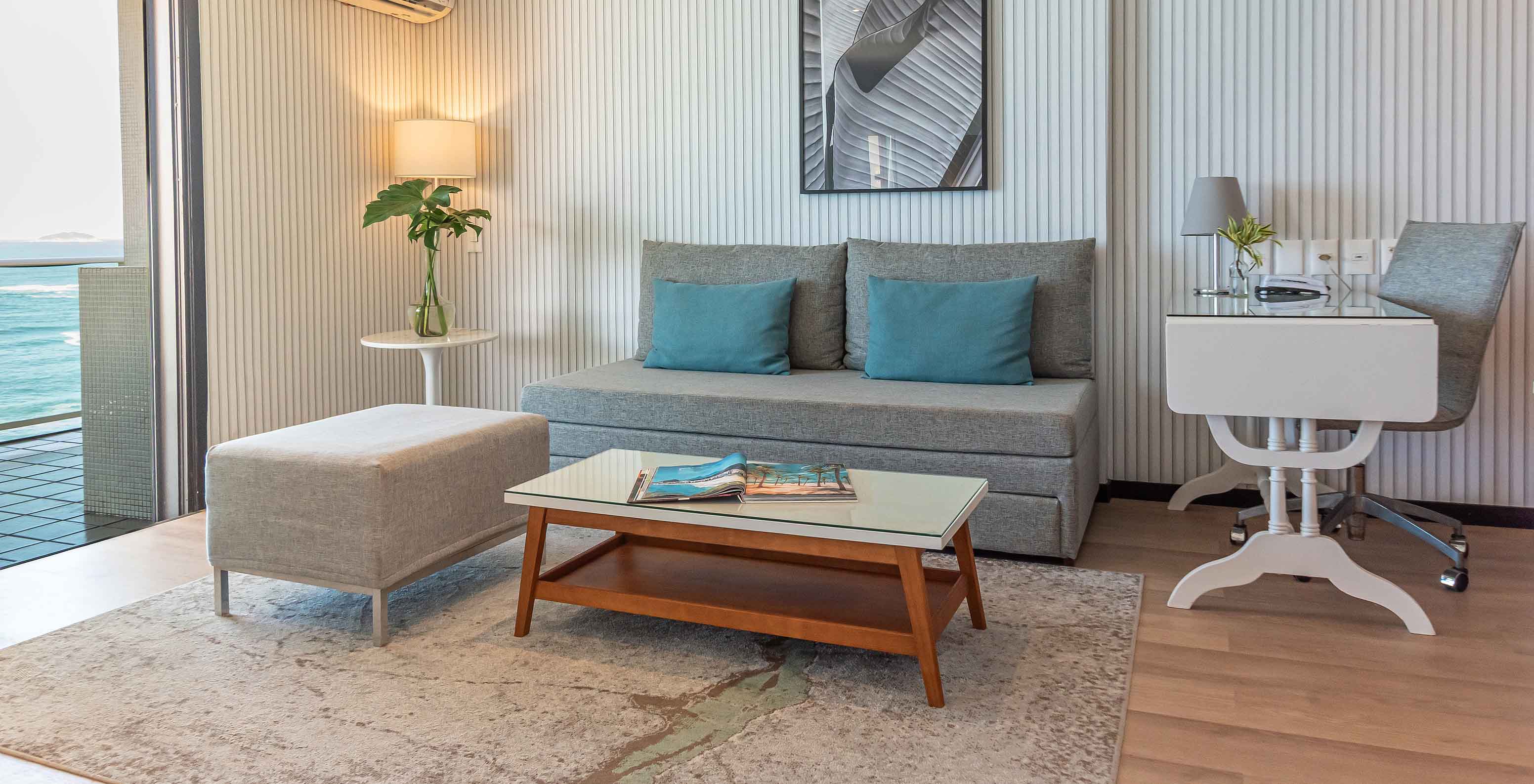 A Suite Frente Praia do Pestana Rio Atlântica tem uma sala moderna com sofá, secretária, mesa de centro e vista para o mar