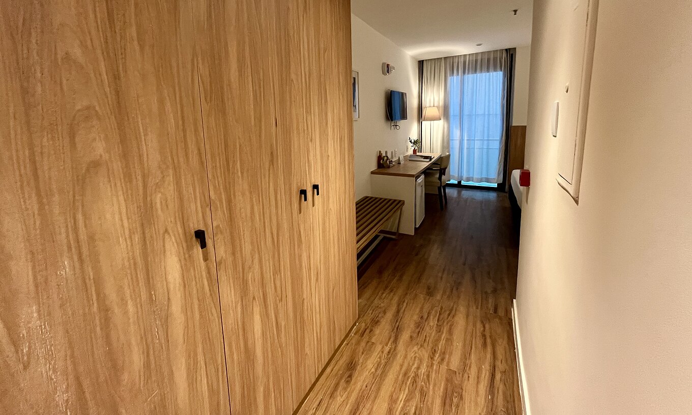 O Quarto Semi Adaptado do Pestana Rio Atlântica tem um corredor com roupeiro de madeira e secretária junto à janela
