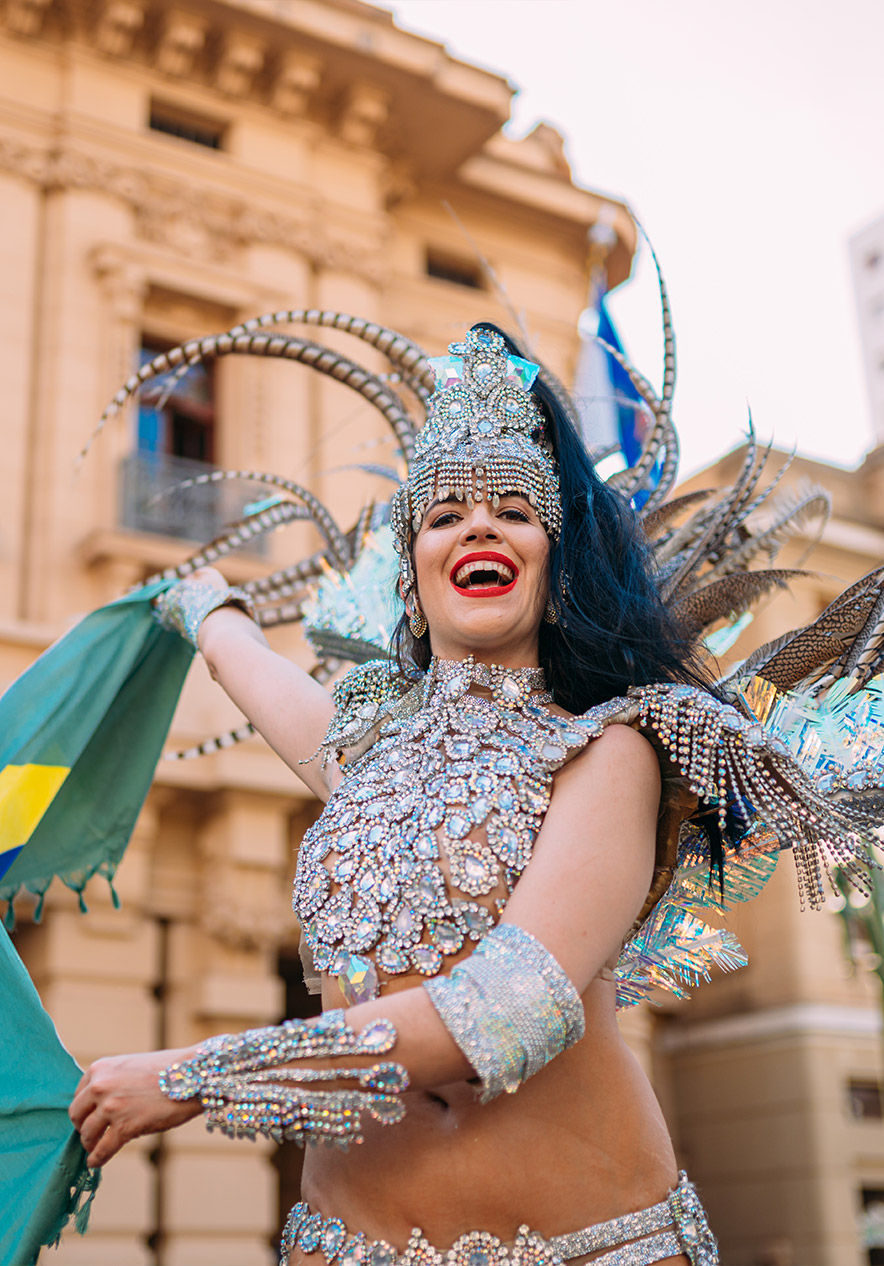 Carnaval no Rio de Janeiro com dançarina em traje brilhante e penas coloridas diante de edifícios históricos