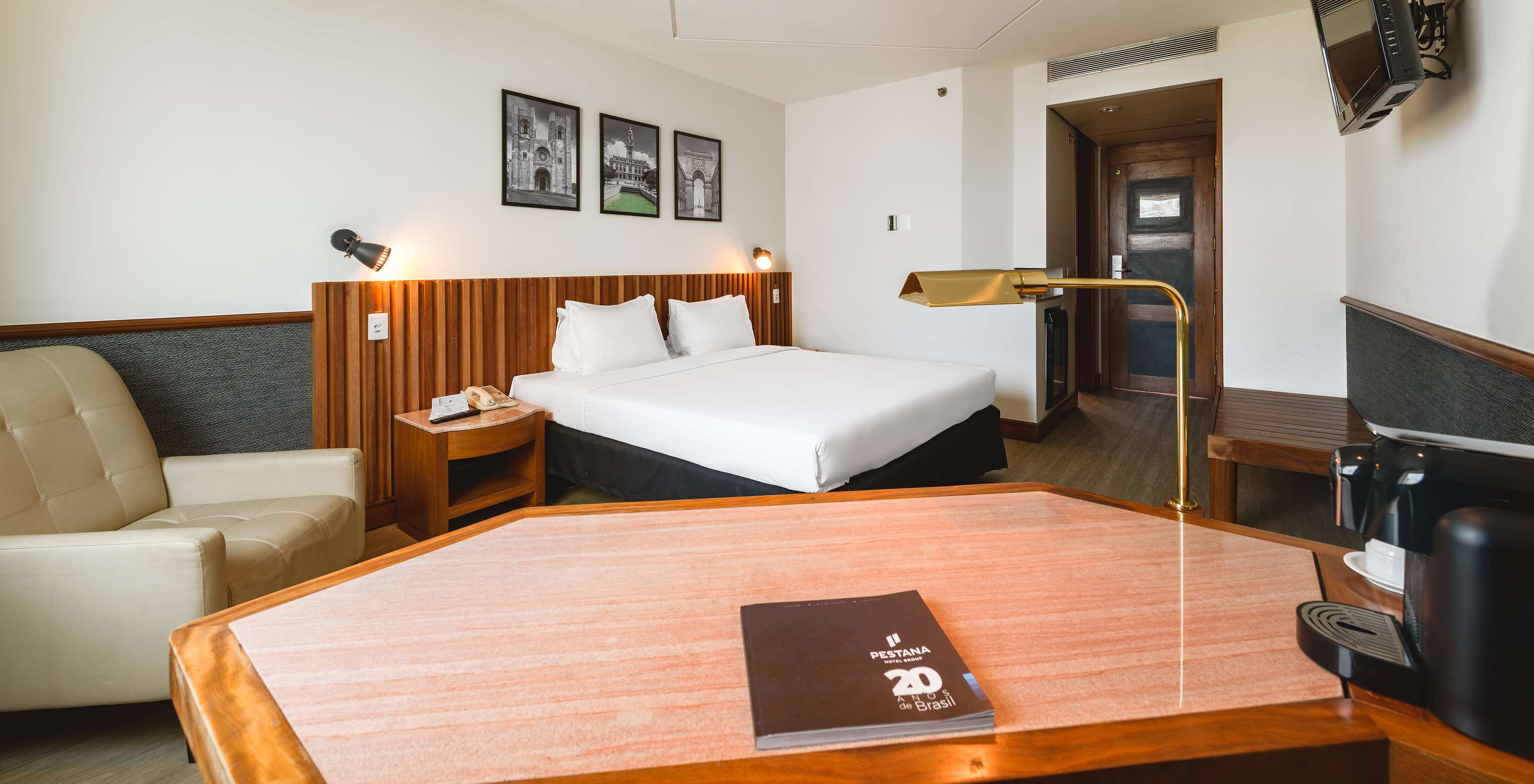 O Queen Superior do Pestana São Paulo tem uma cama de casal, televisão, poltrona e uma secretária com um candeeiro em dourado