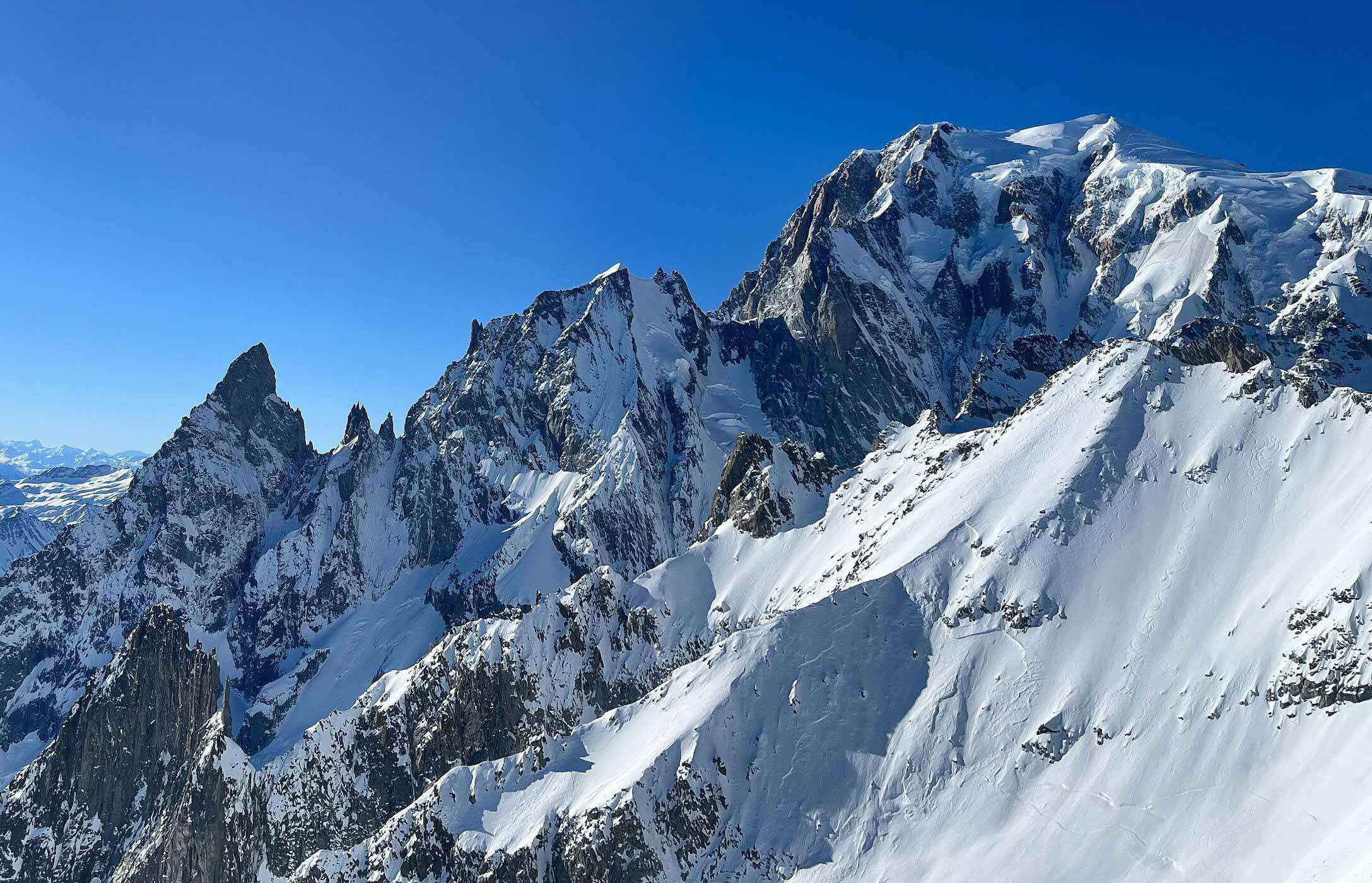 Picos cobertos de neve no maciço do Mont Blanc sob céu azul intenso, com encostas rochosas íngremes