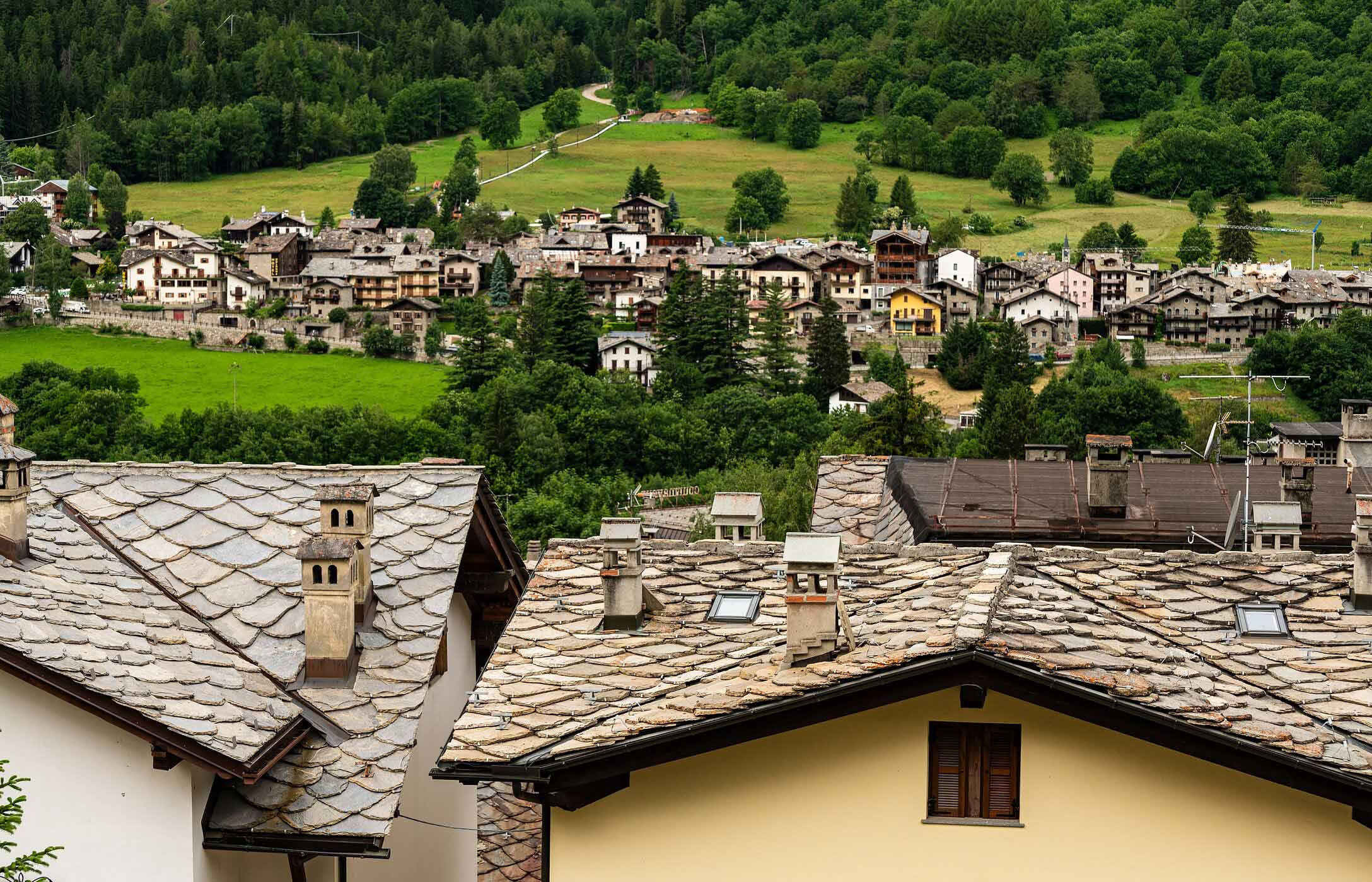 Vista da vila de Courmayeur com telhados de pedra, casas alpinas e encostas verdes cobertas por árvores