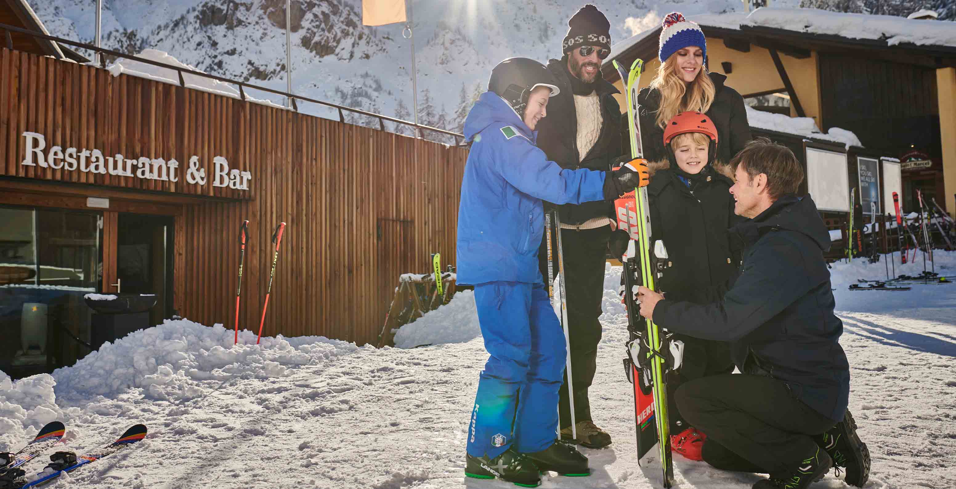 Família com equipamento de esqui em frente a restaurante e bar de madeira perto do Le Massif Courmayeur