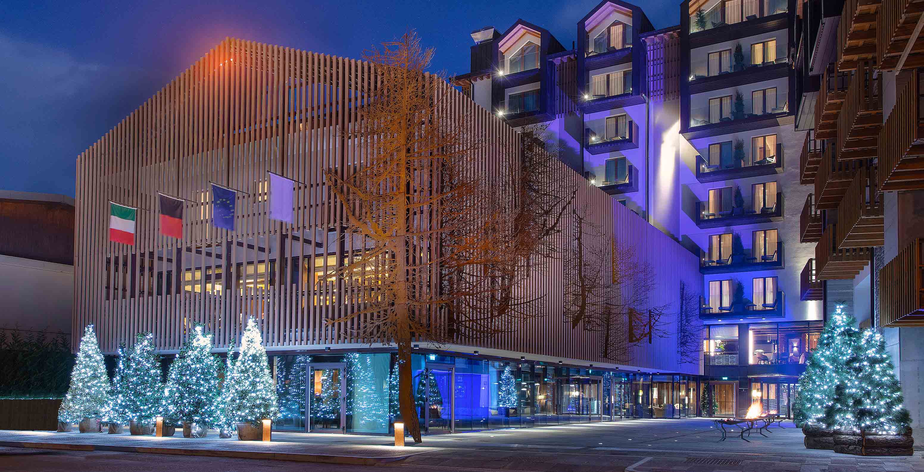 Fachada do Le Massif Courmayeur, Hotel nos Alpes Italianos em Courmayeur para fazer ski, iluminada à noite com árvores decoradas