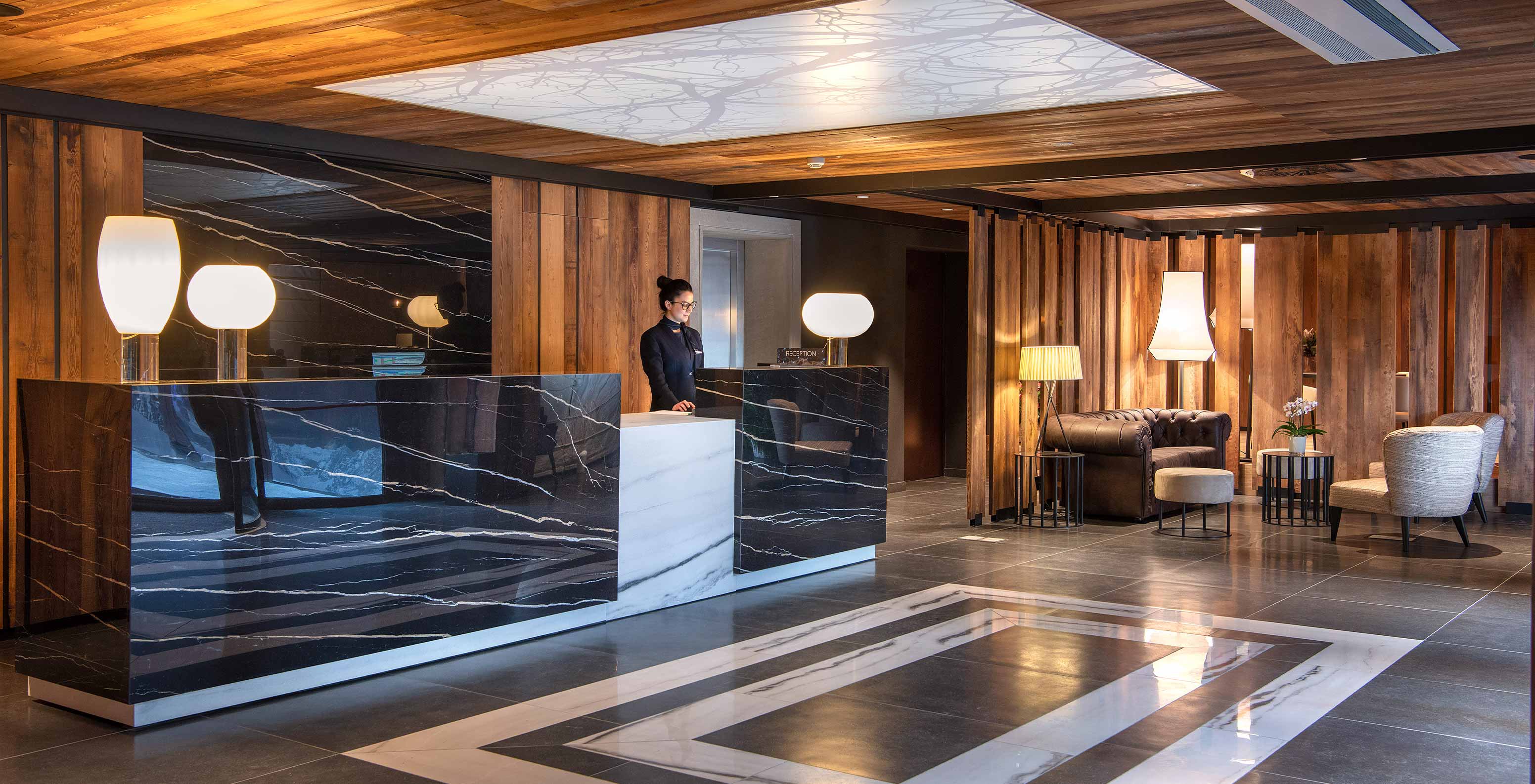 Receção do Le Massif Courmayeur, Hotel nos Alpes Italianos em Courmayeur para fazer ski, com balcão de mármore e área de espera elegante