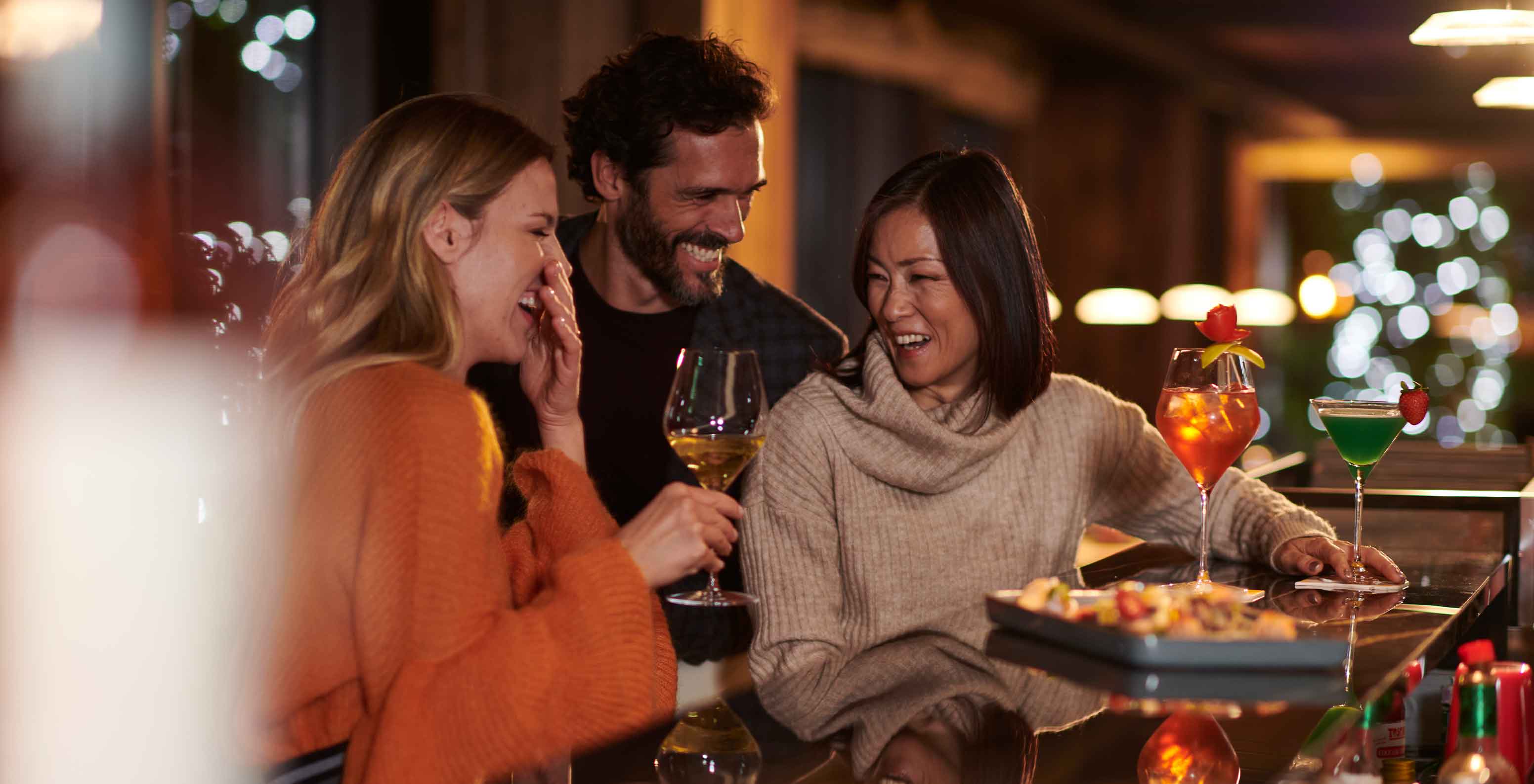 Bar do Le Massif Courmayeur, Hotel nos Alpes Italianos em Courmayeur para fazer ski, com pessoas a conversar e cocktails coloridos sobre o balcão