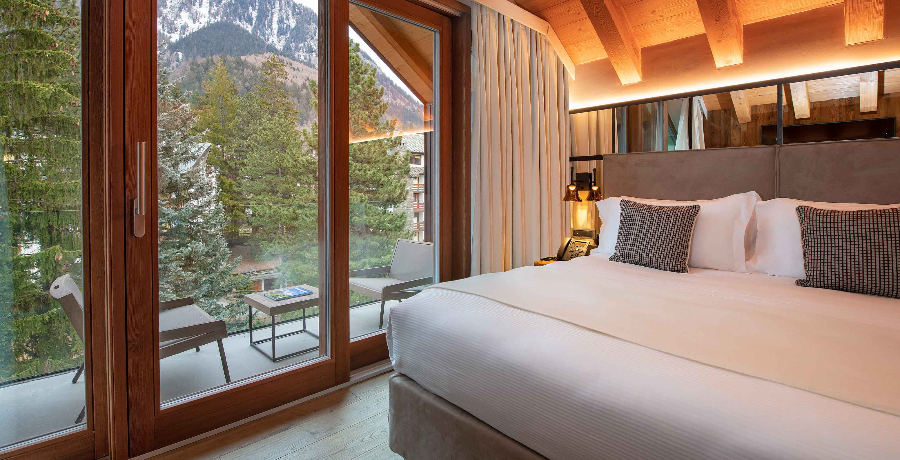 Quarto do Le Massif Courmayeur com cama grande, almofadas e varanda com vista para montanhas e árvores