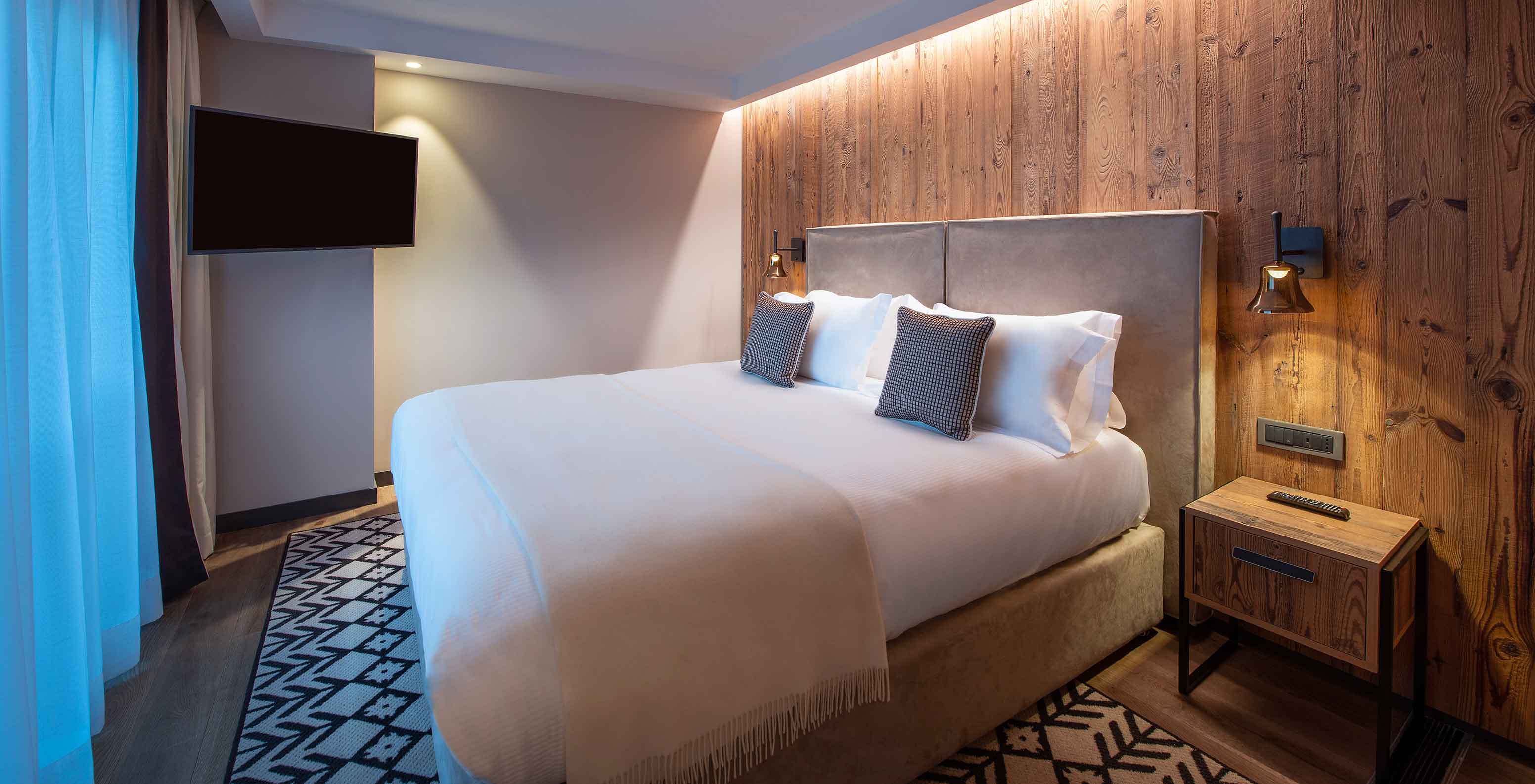 Quarto do Le Massif Courmayeur, Hotel nos Alpes Italianos, com cama grande, parede de madeira e iluminação suave