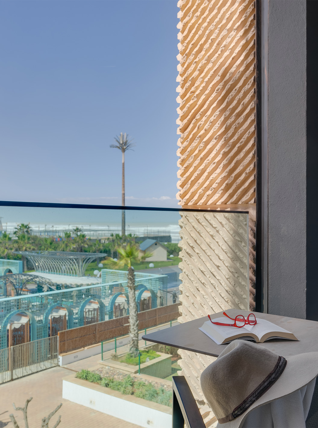Suite no Pestana Casablanca com varanda mobilada e vista sobre jardins, palmeiras e o mar ao fundo