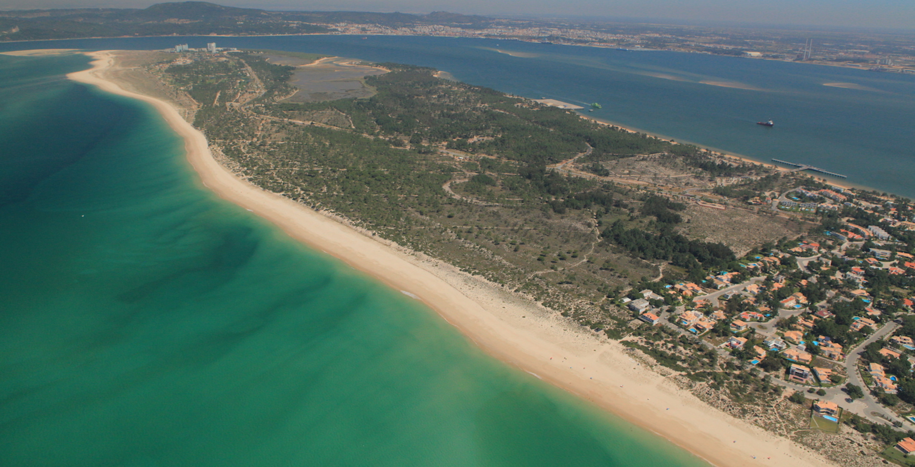 Vista aérea para a Península de Tróia, com água transparente com muita vegetação pelo meio e várias casas com piscina