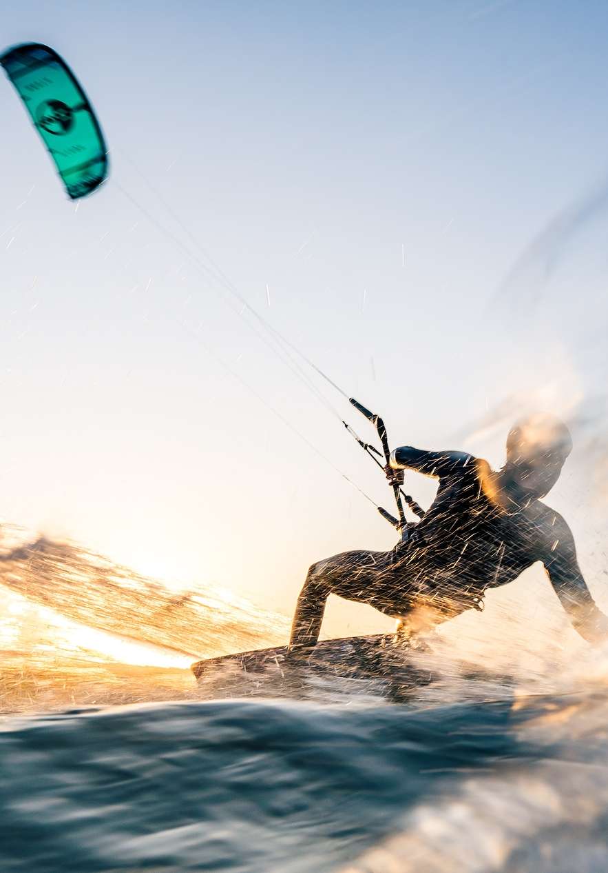 Pessoa a fazer Kitesurf numa praia num dia de sol, com céu azul e água clara
