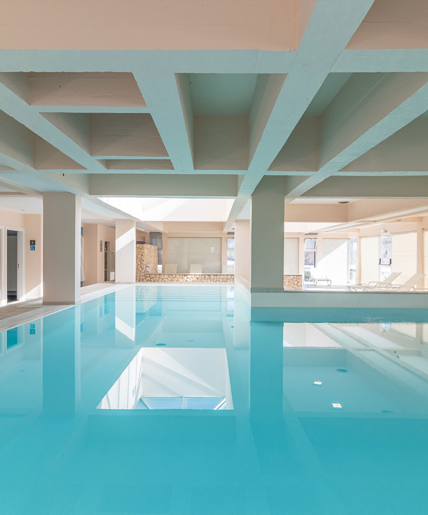 Piscina interior com luz natural e espreguiçadeiras no aparthotel em frente ao mar
