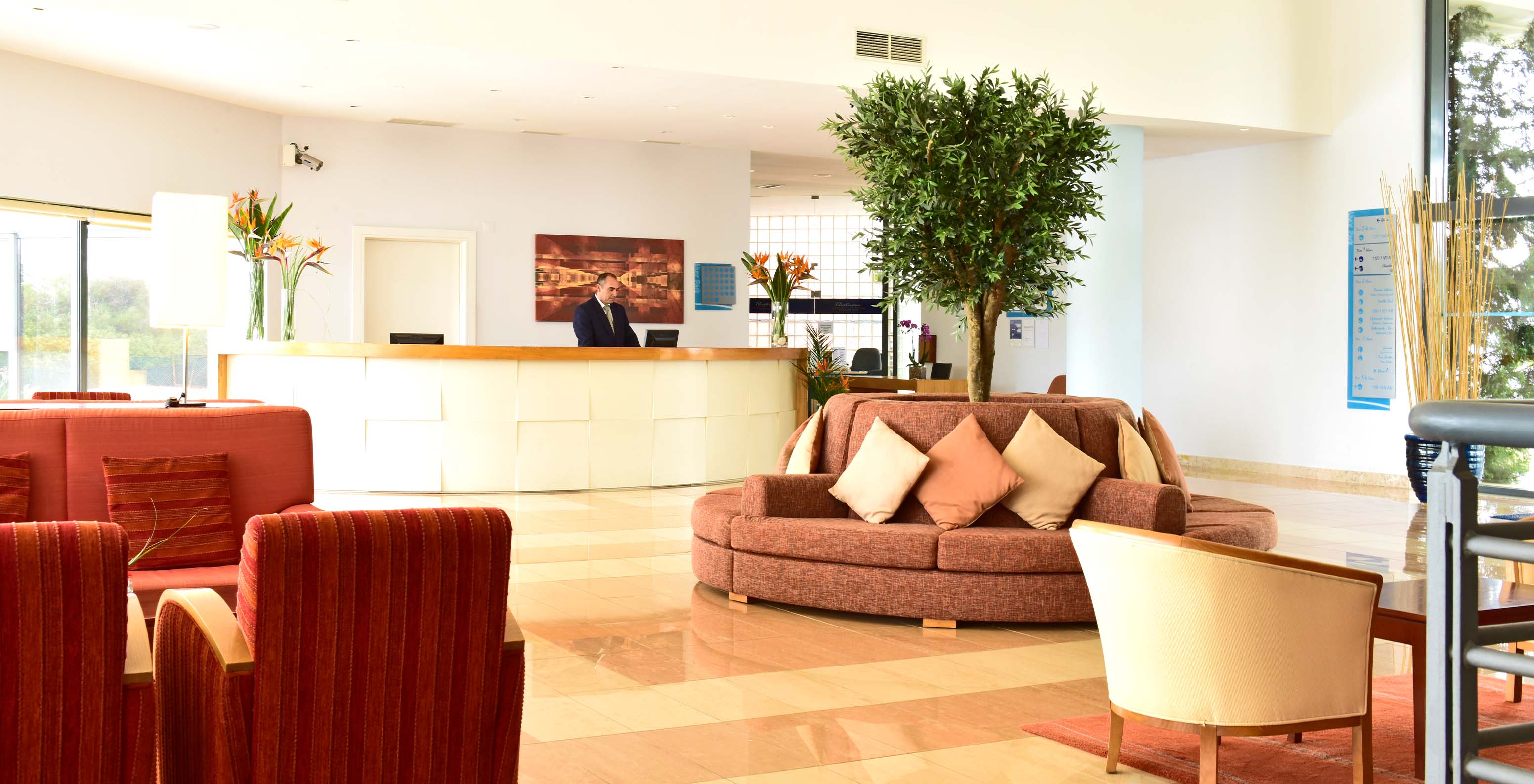 Receção do hotel Pestana Alvor Park, com sofás e cadeirões vermelhos, com flores em vasos e uma árvore no centro