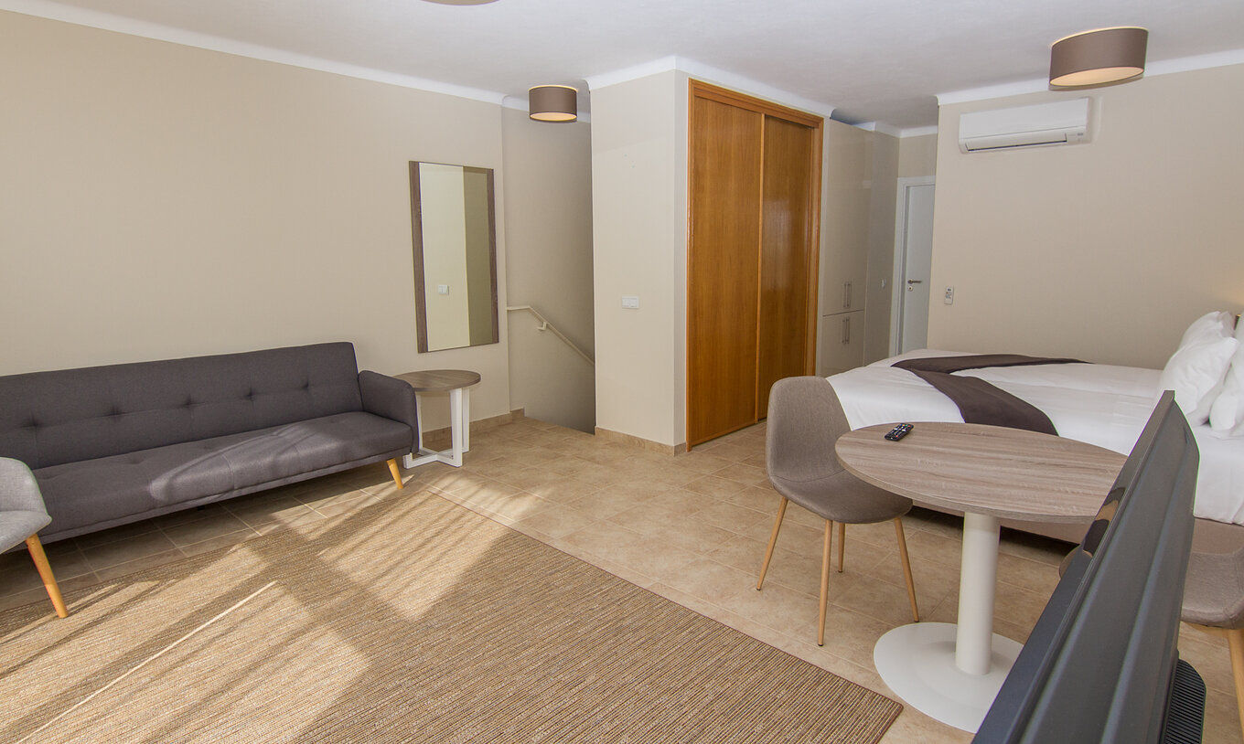 O Studio do Pestana Gramacho Residences tem um sofá grande, uma mesa e uma cadeira, ar condicionado e um armário na parede