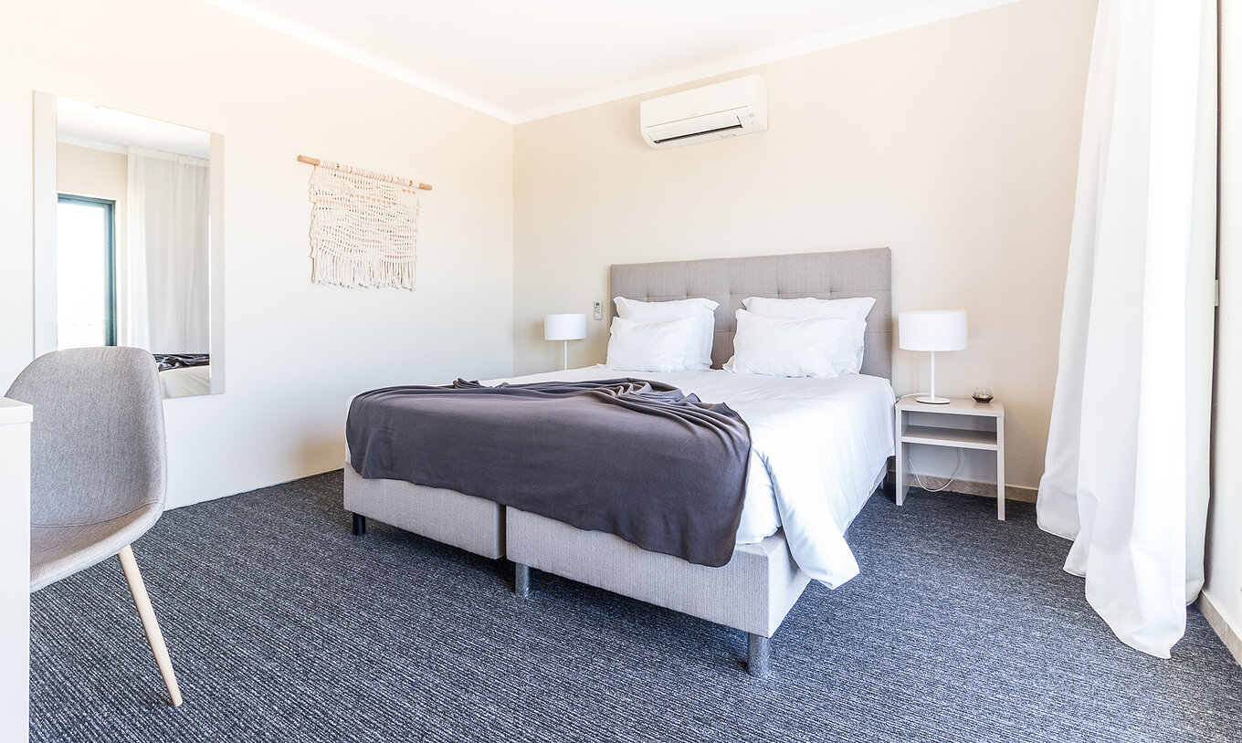 O Apartamento T2 do Pestana Gramacho Residences tem um quarto moderno com cama, ar condicionado e decoração minimalista