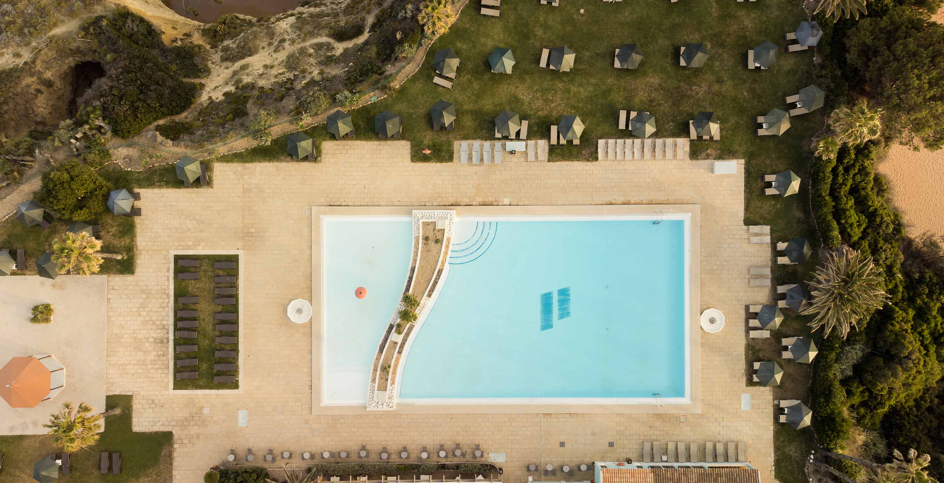 Piscina exterior do Pestana Viking, rodeada de vegetação, com várias espreguiçadeiras com chapéu de sol