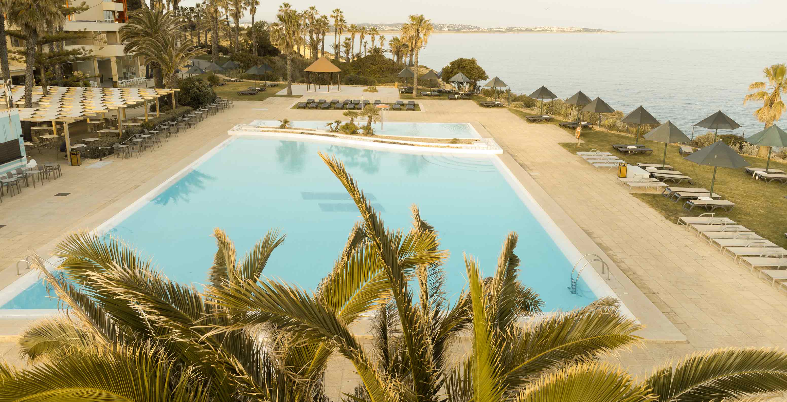 Piscina exterior do Pestana Viking, com várias palmeiras, espreguiçadeiras e com vista para o mar