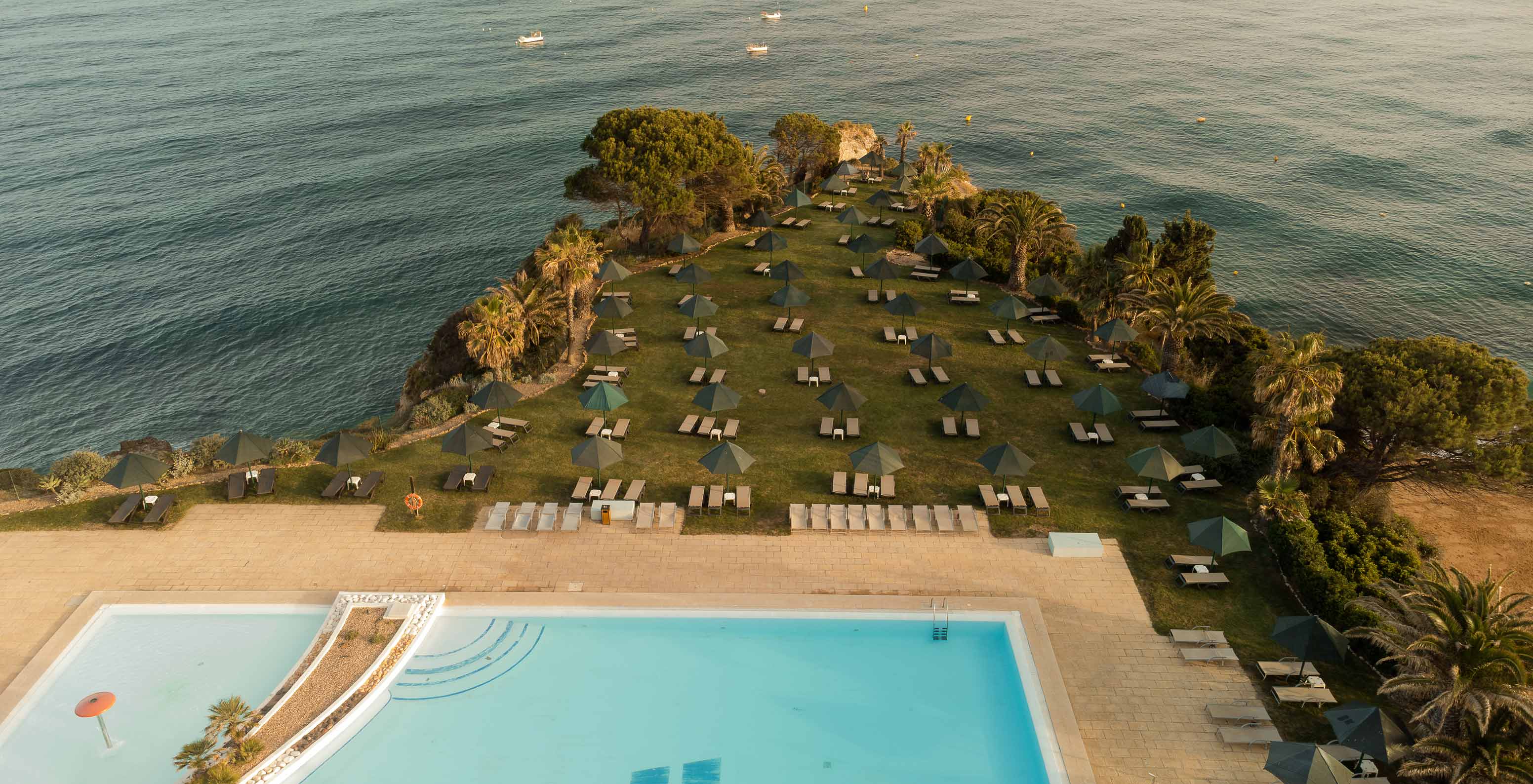Piscina exterior do Pestana Viking, com espreguiçadeiras, e rodeada de vegetação, com vista para o mar