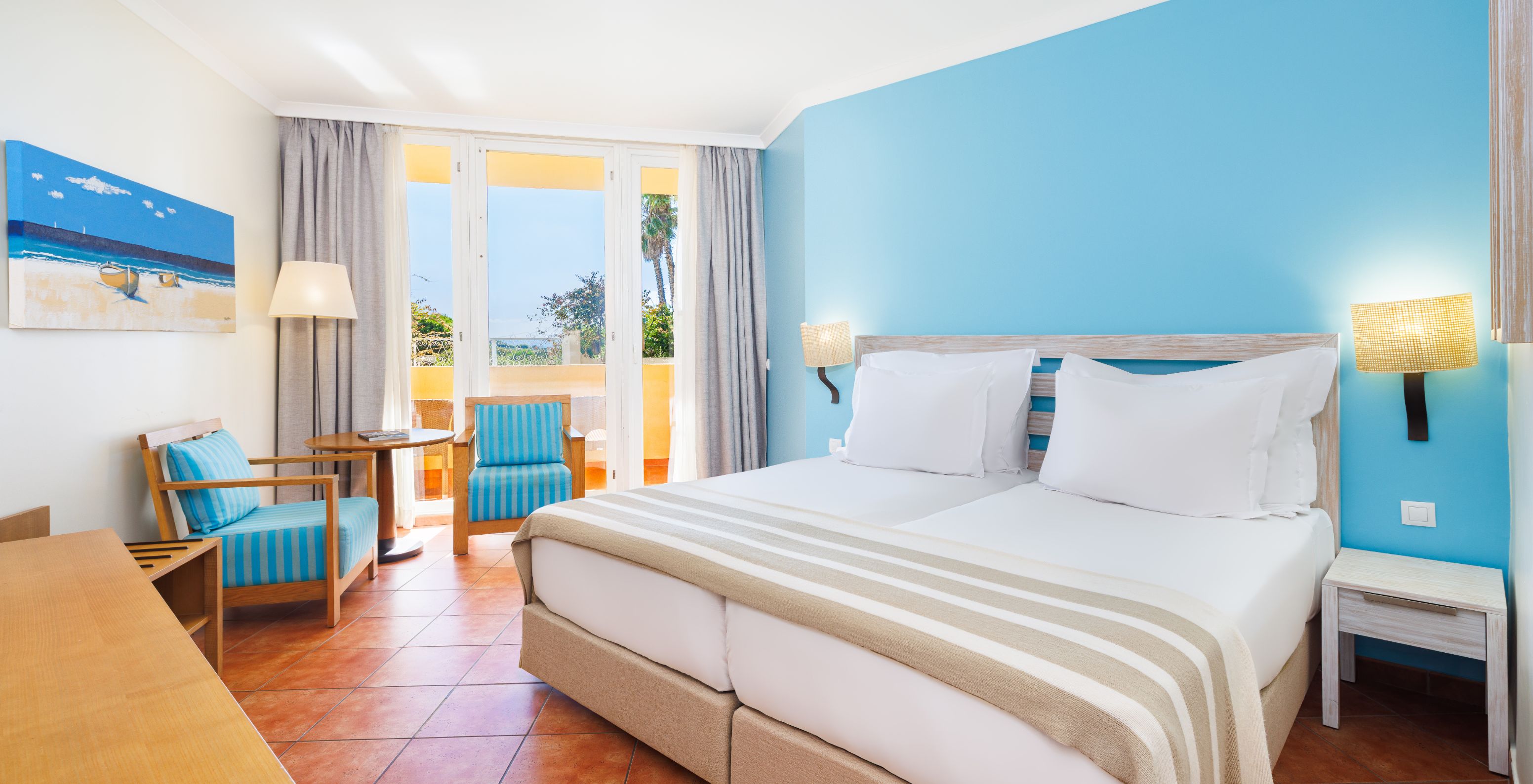 Quarto Deluxe Vista Jardim no Pestana Viking com cama dupla, poltronas azuis e varanda com luz natural