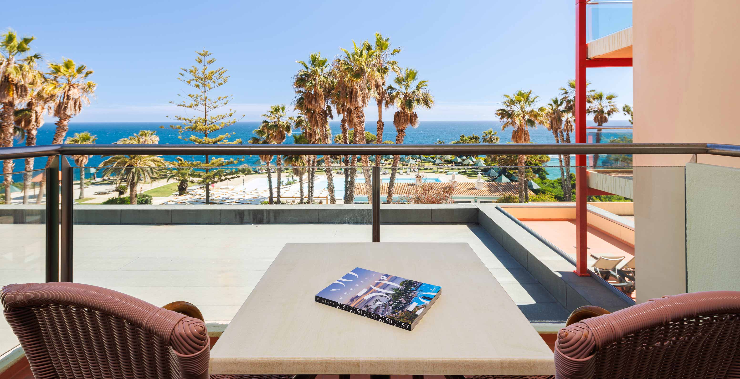 Suite com Vista Mar e Varanda no Pestana Viking, apresentando terraço amplo com palmeiras e oceano ao fundo