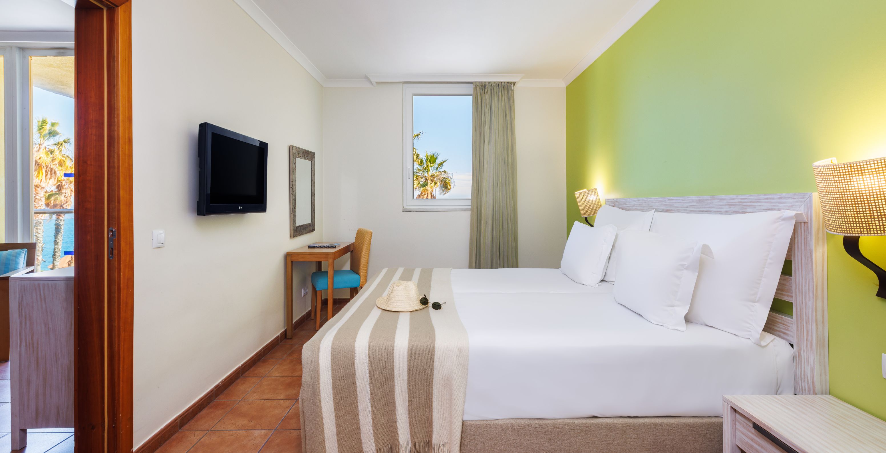 Suite com Vista Mar no Pestana Viking com cama de casal, secretária em madeira e janela com palmeiras