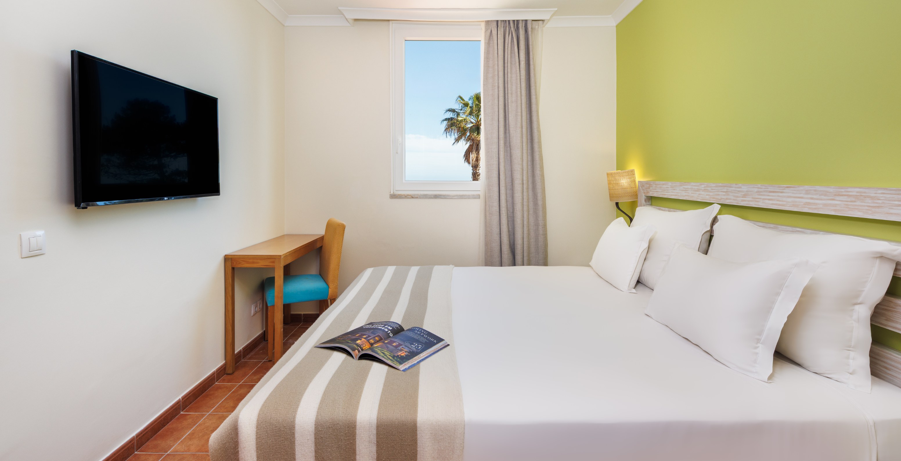 Suite T2 no Pestana Viking com cama de casal, secretária em madeira e janela com vista para palmeiras