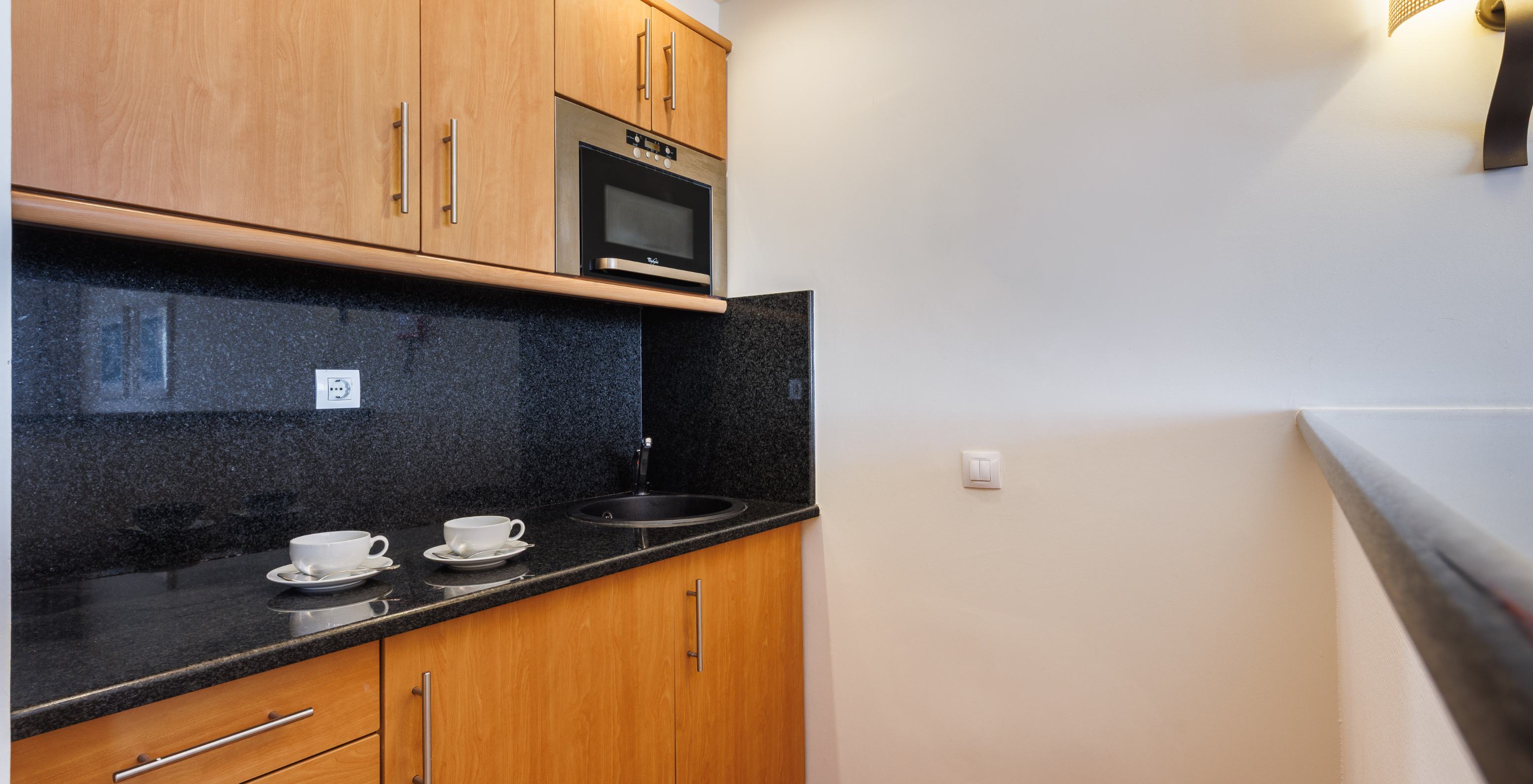 Suite T2 no Pestana Viking com kitchenette em madeira, bancada preta, micro-ondas embutido e chávenas