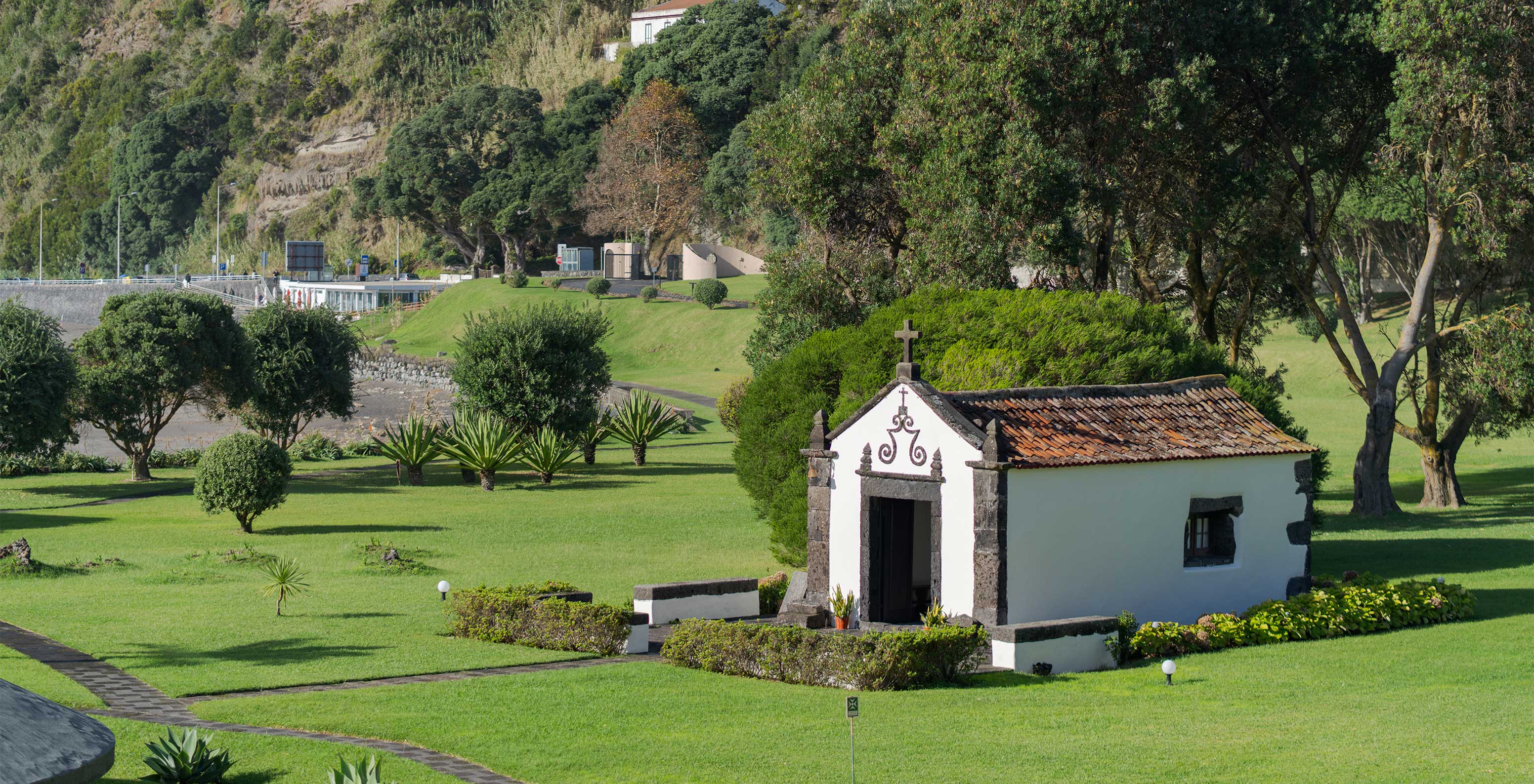 Capela no exterior do hotel, no meio de jardins verdes com árvores e pequenos passeios onde o cliente pode passear