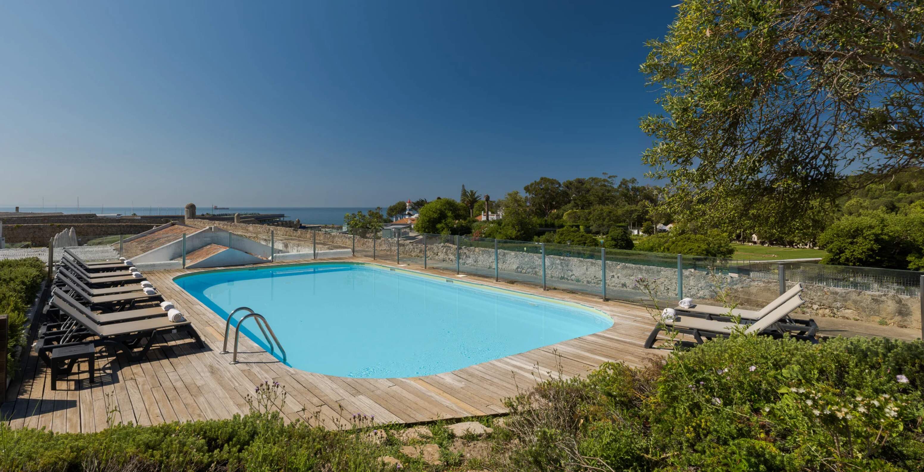Piscina exterior junto ao mar perto do Pestana Cidadela Cascais hotel, com espreguiçadeiras e jardins