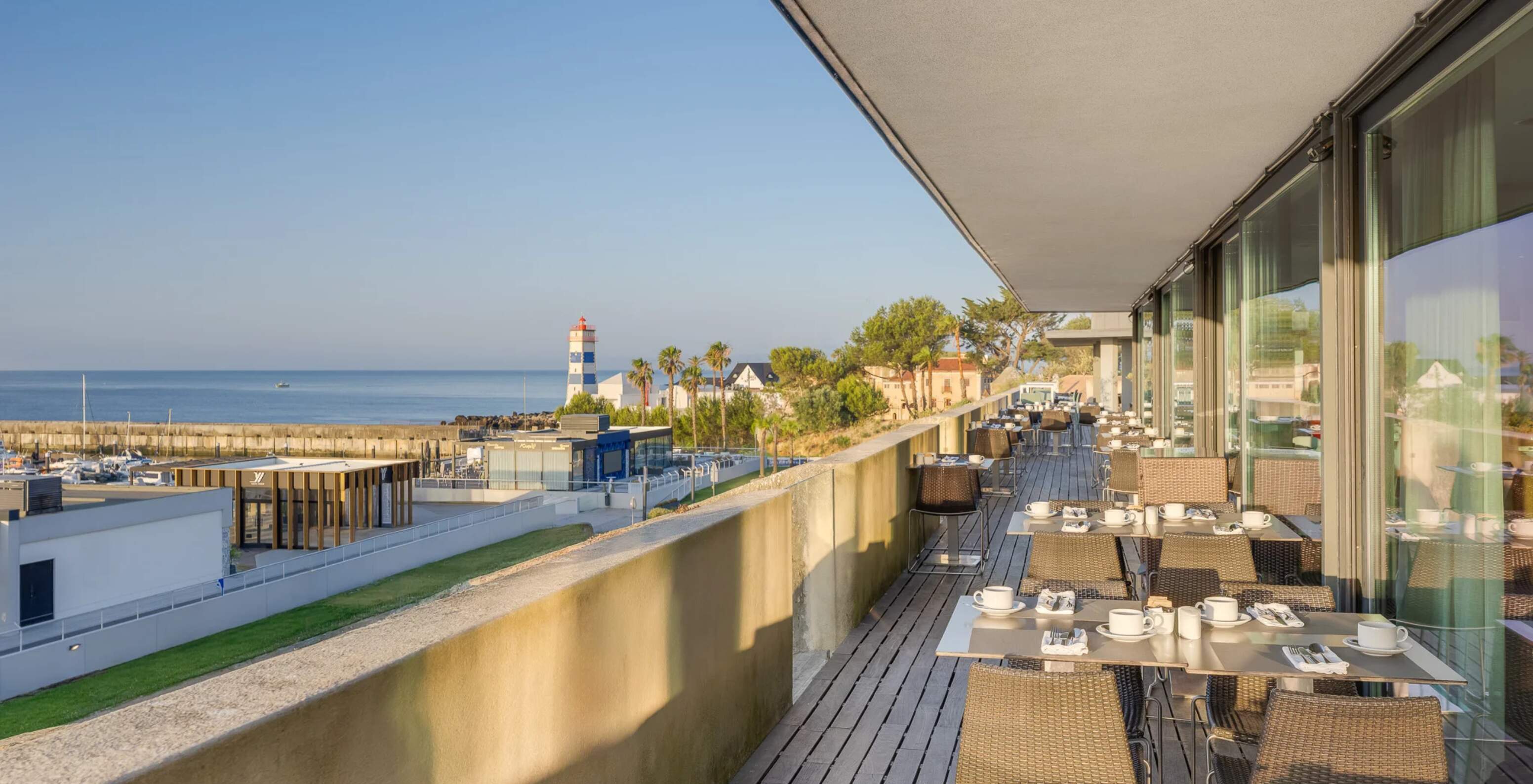 Pestana Cidadela Cascais Hotel 5 Estrelas em Cascais, terraço com mesas e vista para o mar e farol costeiro ao entardecer