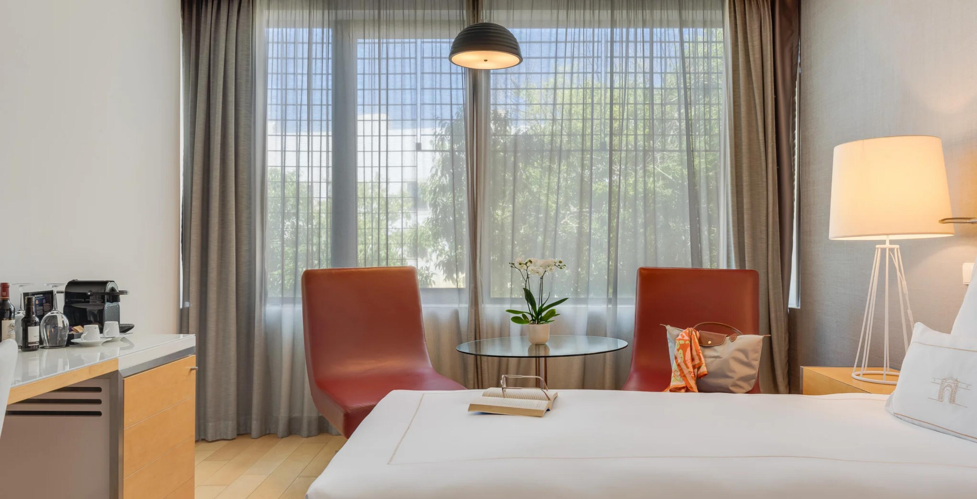 Hotel Pestana Cidadela Cascais com quarto luminoso, poltronas vermelhas e janela ampla com cortinas