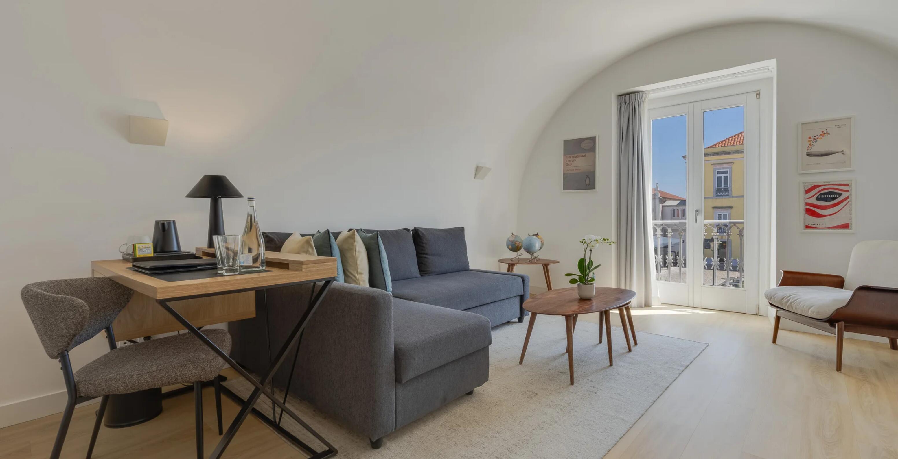 Pestana Cidadela Cascais hotel com sala luminosa, sofá cinzento, mesa de madeira e varanda com vista urbana