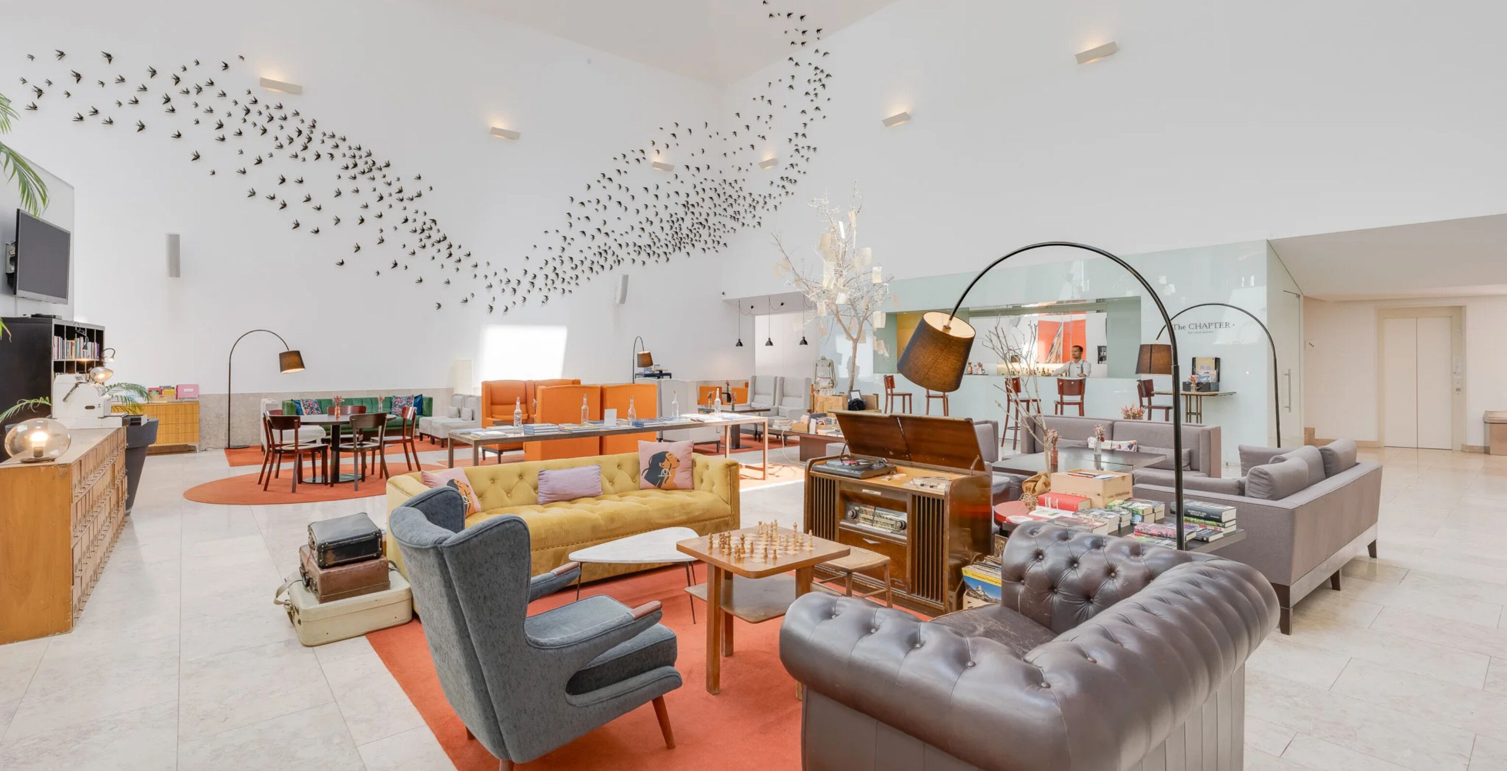 Salão amplo com sofás, mesas e iluminação moderna, destacando decoração artística com aves na parede