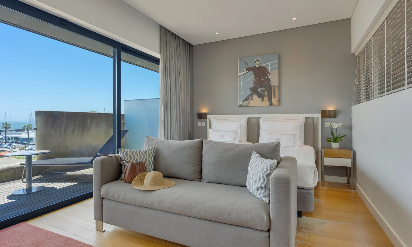 Quarto moderno com cama de casal, sofá cinzento e varanda com vista para o mar e marina de Cascais