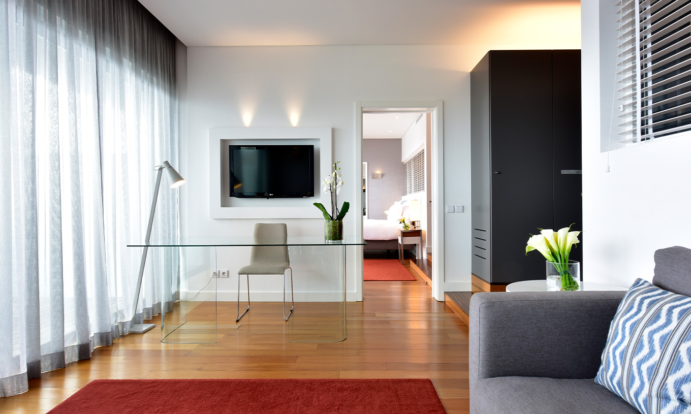 A Suite do Pestana Cidadela Cascais tem uma sala de estar com sofá cinzento, televisão, secretária e mesa